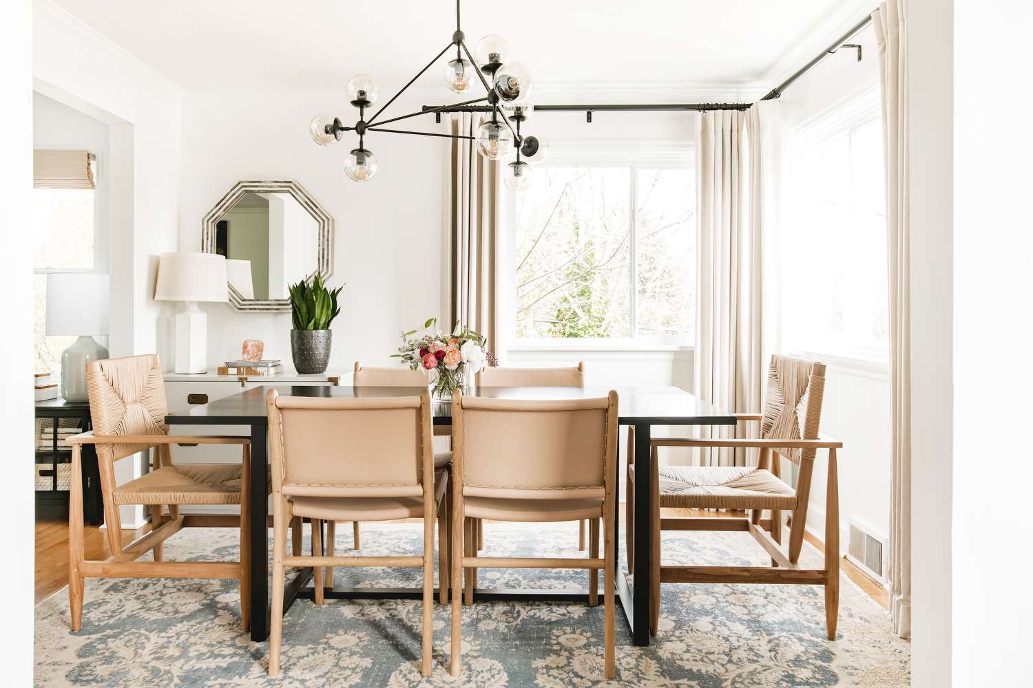 Sala de jantar com cadeiras de madeira clara e lustre preto.