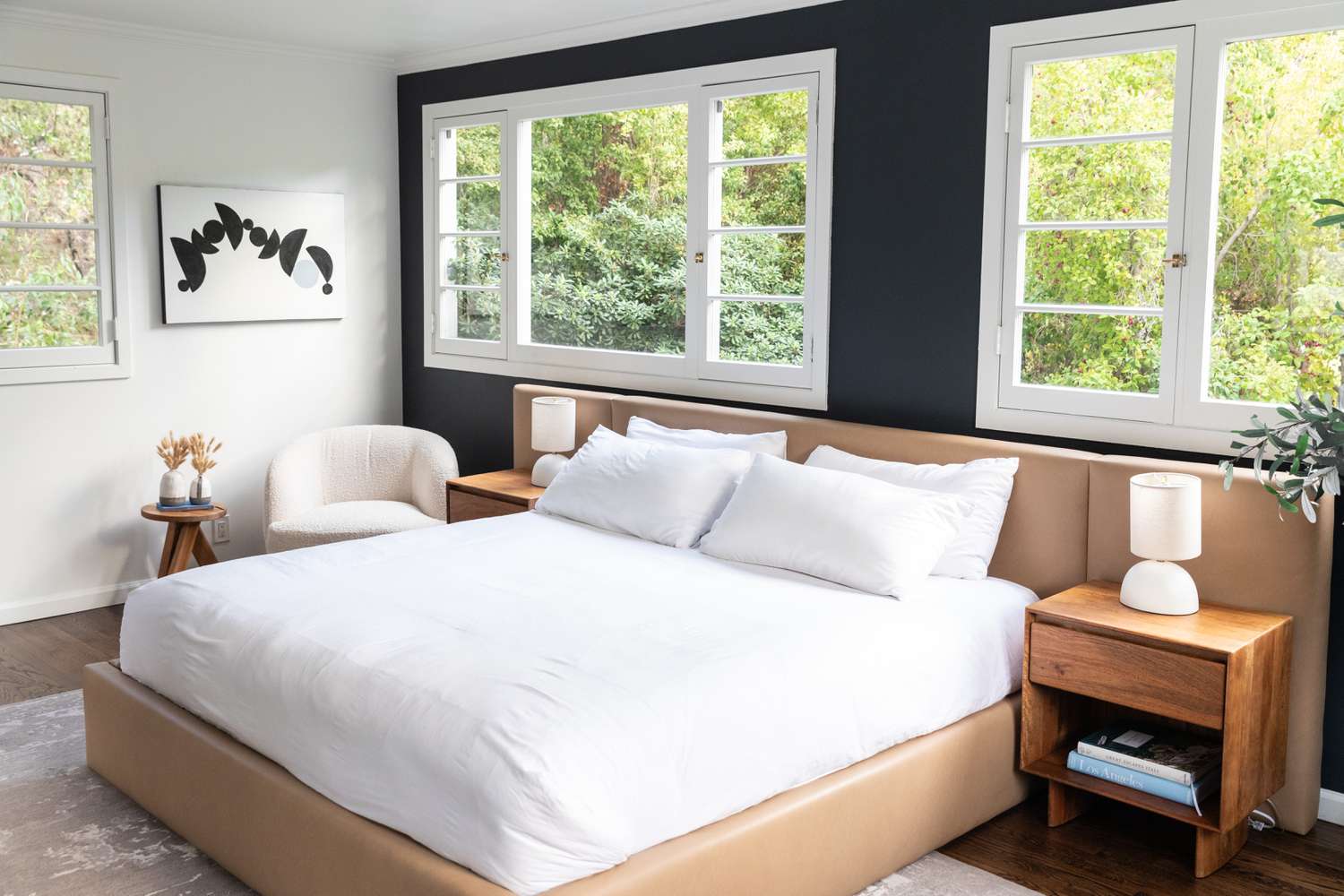 Schlafzimmer mit dunkler Akzentwand hinter weiß gepolstertem Bett und breiten Fenstern