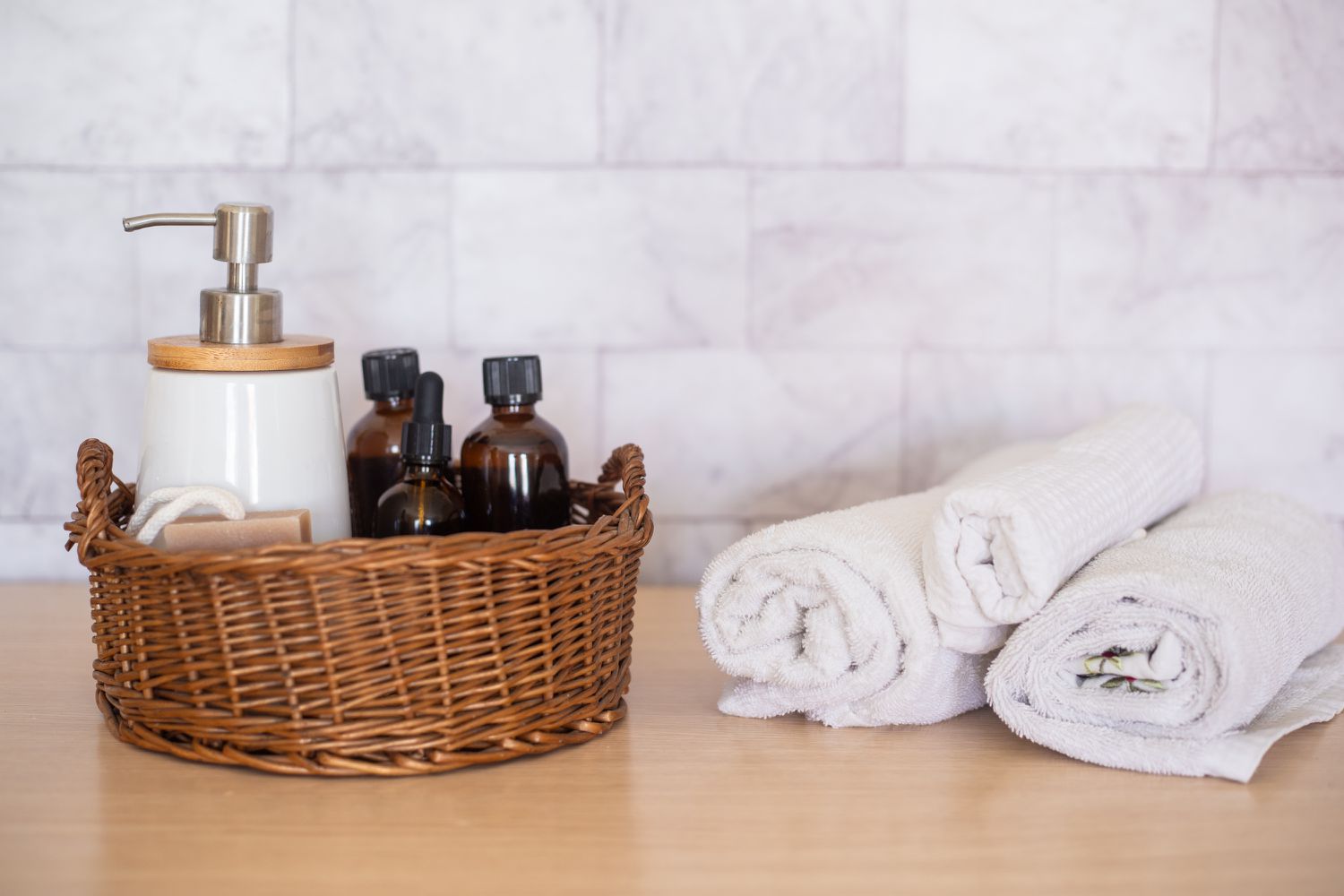 Bathroom essentials placed in wicker basket next to rolled towels