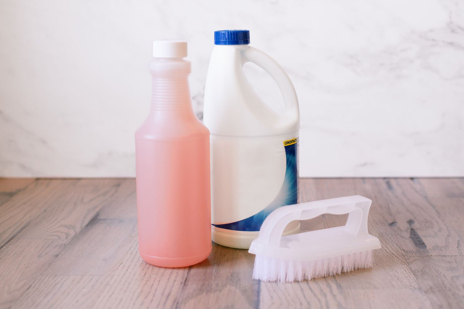 Bouteille de solution d'eau TSP à côté d'une brosse rigide et d'une bouteille d'eau de Javel sur un plancher en bois