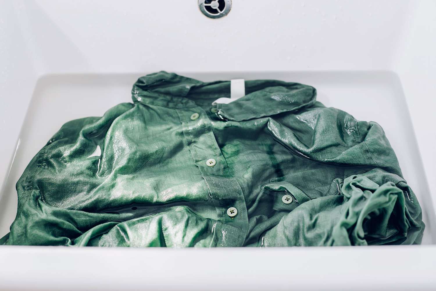 Camisa verde colocada en el fregadero y remojada en agua con solución de lejía oxigenada