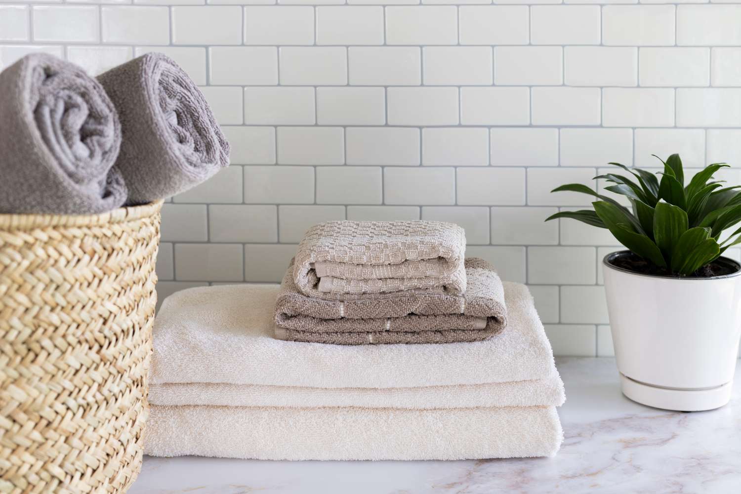 Serviettes blanches et bronzées pliées dans la salle de bain à côté d'une plante d'intérieur et d'un panier en osier avec des serviettes grises roulées