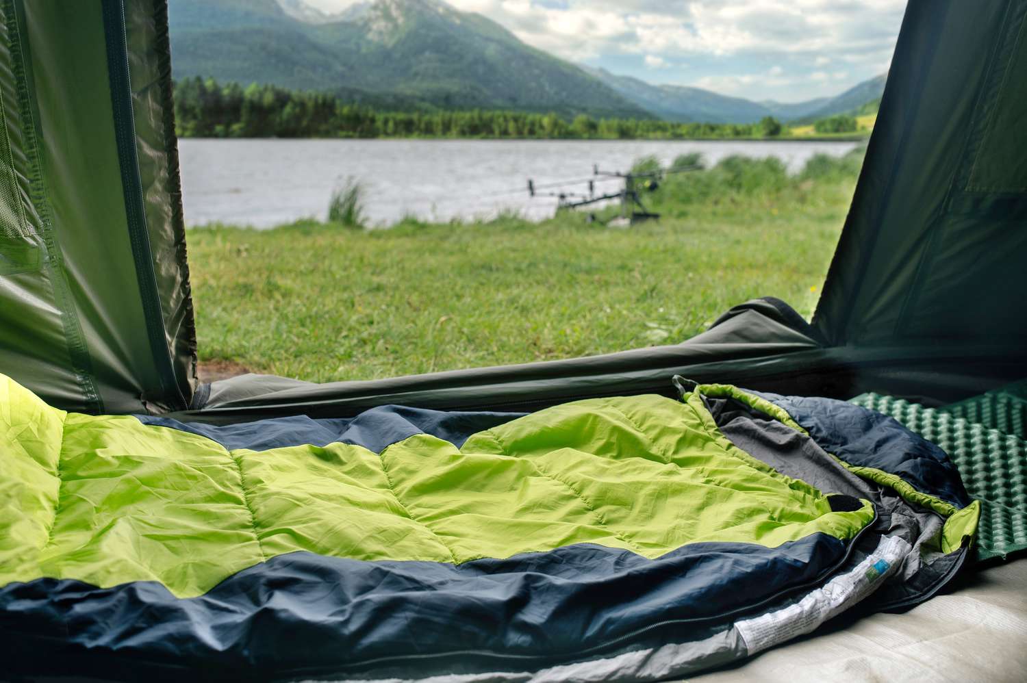 Grüner und blauer Schlafsack im Zelt mit offener Tür am See