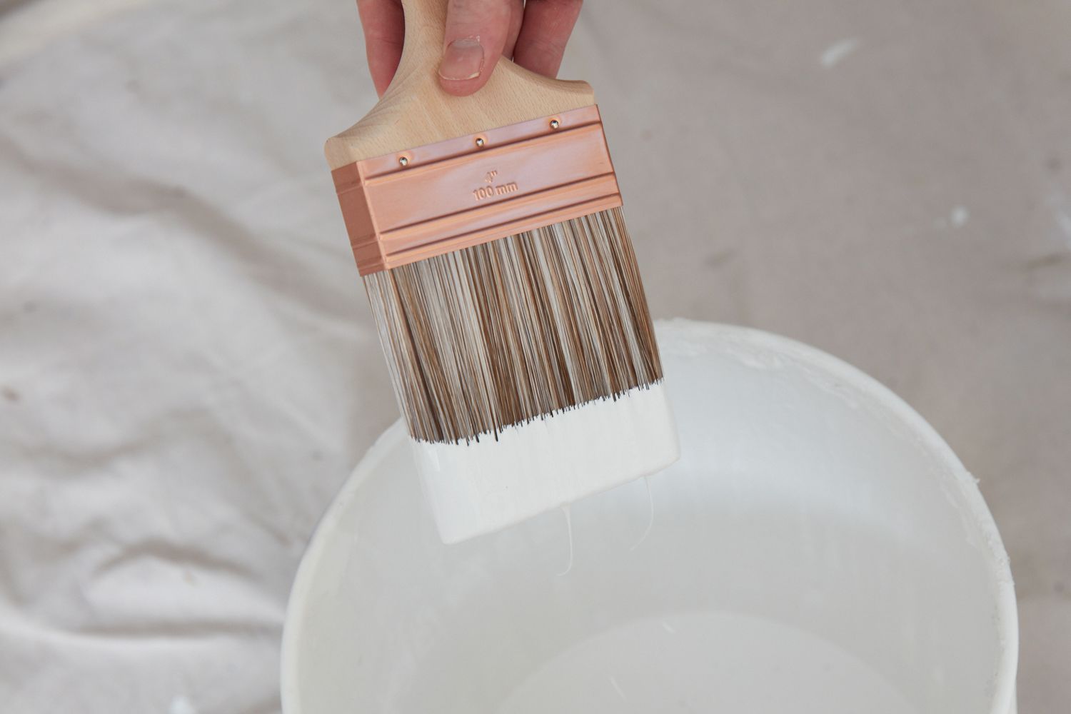 Paint brush dipped in white paint over bucket