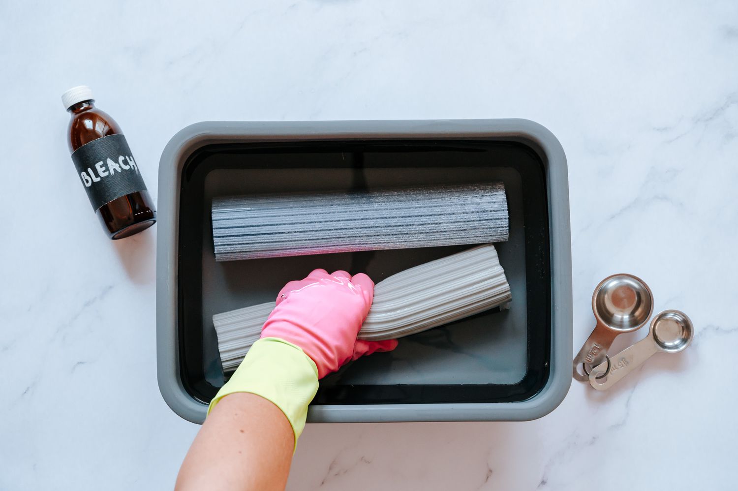 Schwammköpfe in grauem Eimer mit Chlorbleiche und heißem Wasser mit rosa Handschuhen gereinigt