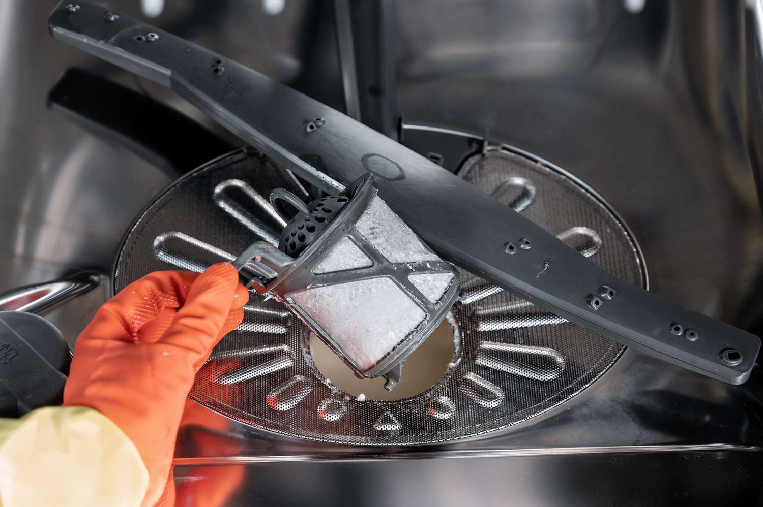 Spülmaschinenfilter mit orangefarbenen Handschuhen aus dem zylindrischen Filter entfernen