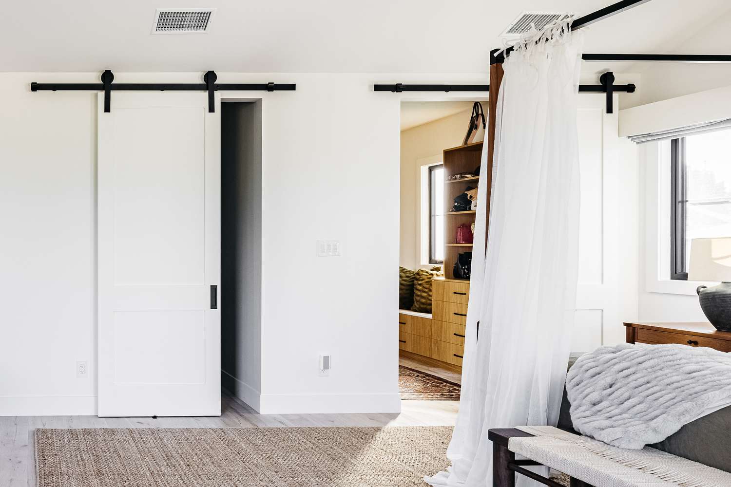 Weißes Scheunentor mit schwarzem Geländer, das einen Schrank in einem großen Schlafzimmer abdeckt
