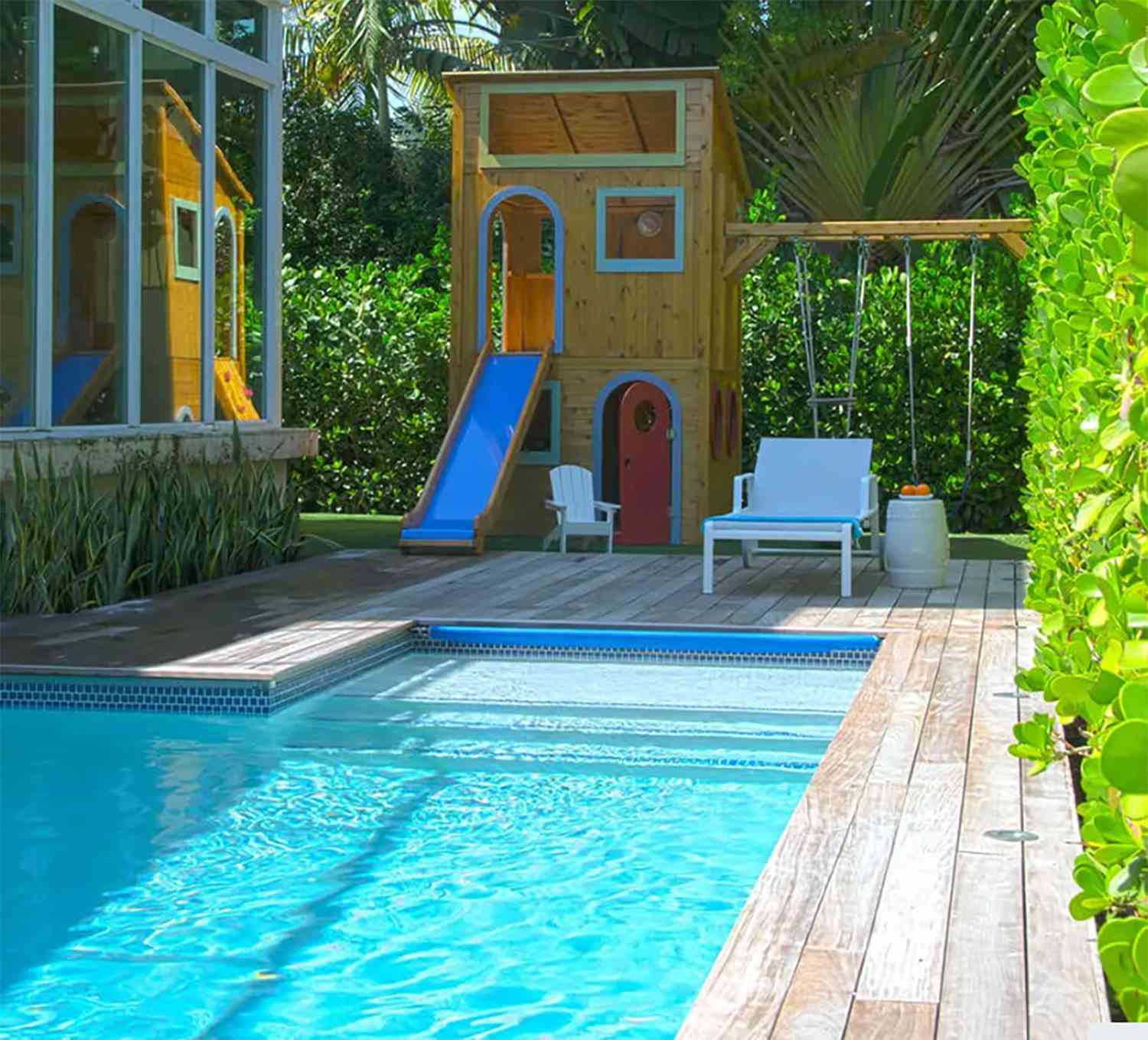 Una piscina en el patio trasero con tarima de madera y columpios para los niños