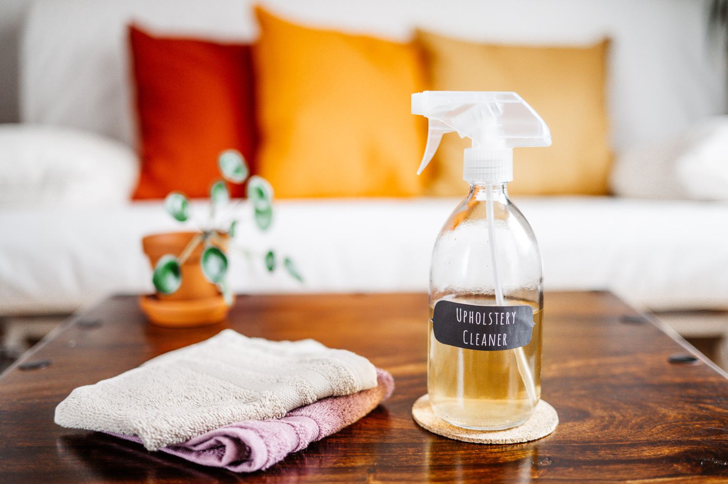 Homemade upholstery cleaner in clear spray bottle next to folded towels