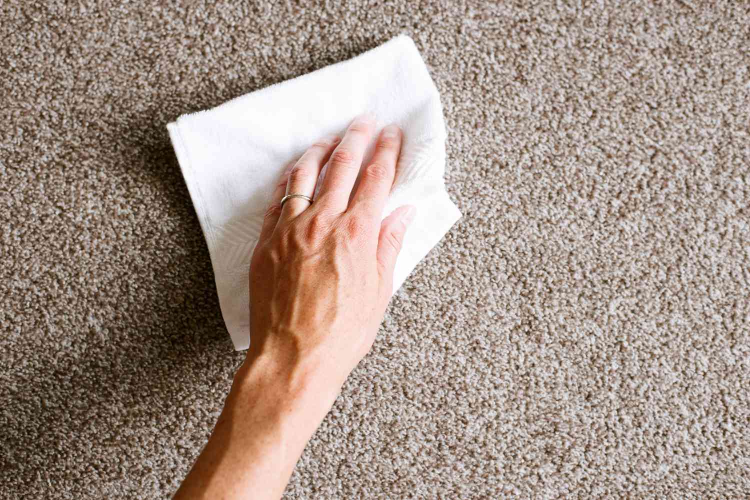 Verschüttete Flüssigkeit auf hellbraunem Teppich mit Papiertuch abgetupft