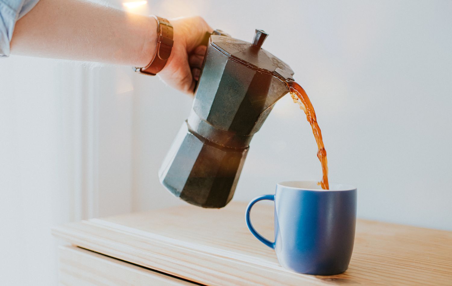 Eine Person gießt Kaffee aus einer Kaffeemaschine in einen Becher.