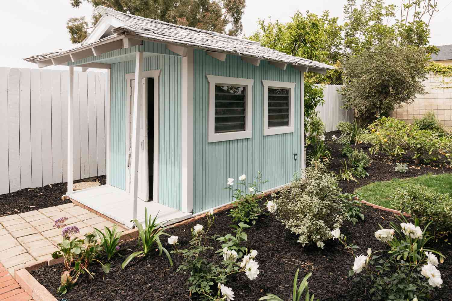 Galpão externo azul bebê e branco próximo ao jardim de flores