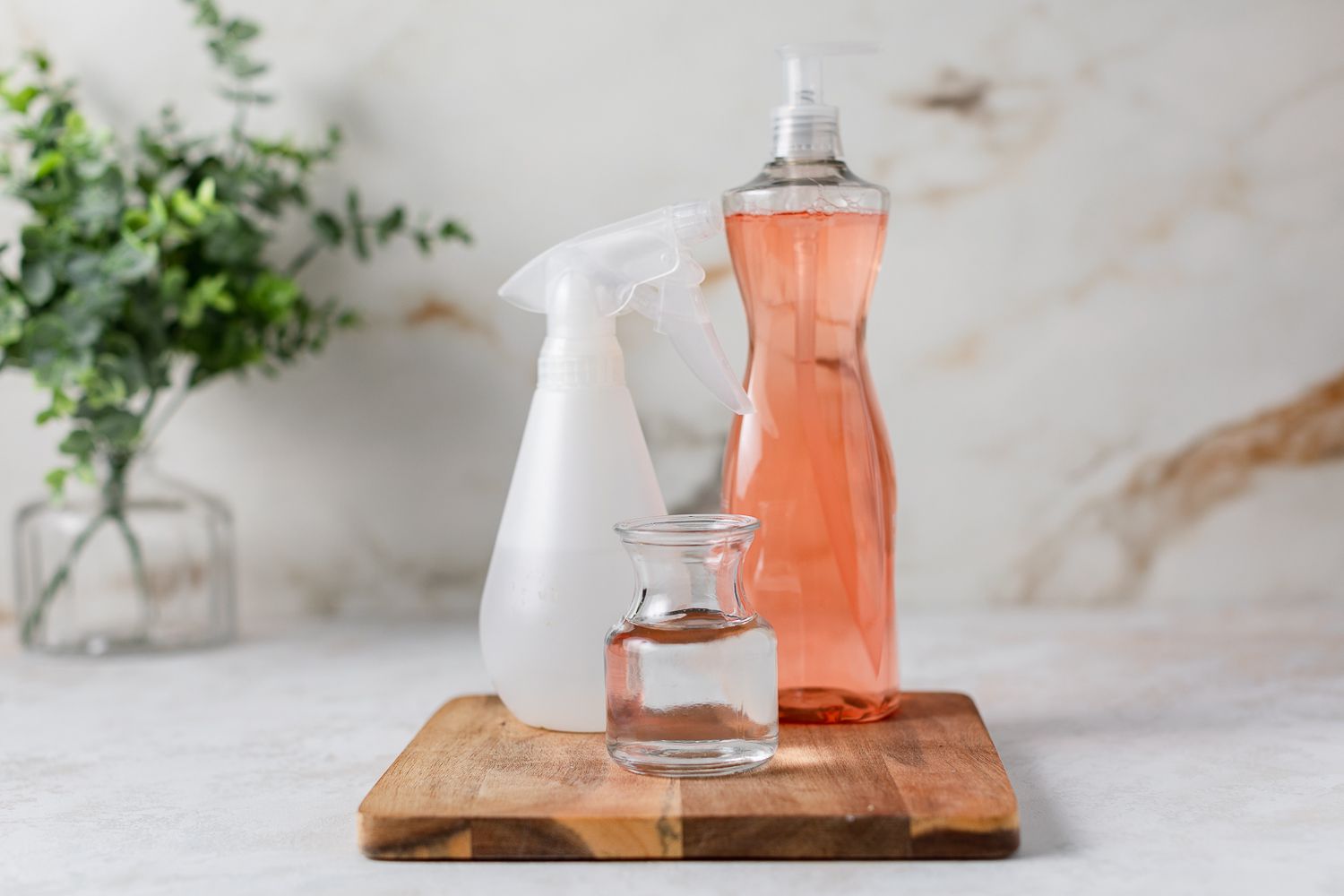 Jabón lavavajillas rosa junto a botella de spray y recipiente de cristal con agua