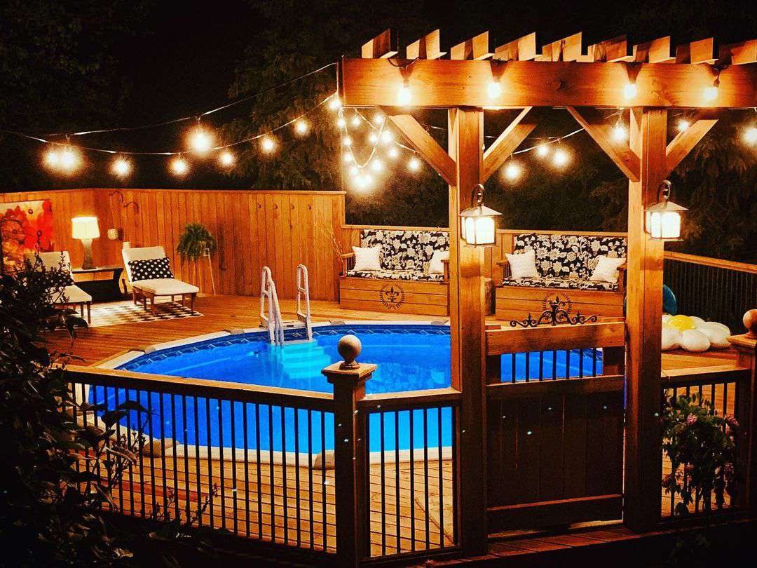 A nighttime view of an above ground pool with a large deck