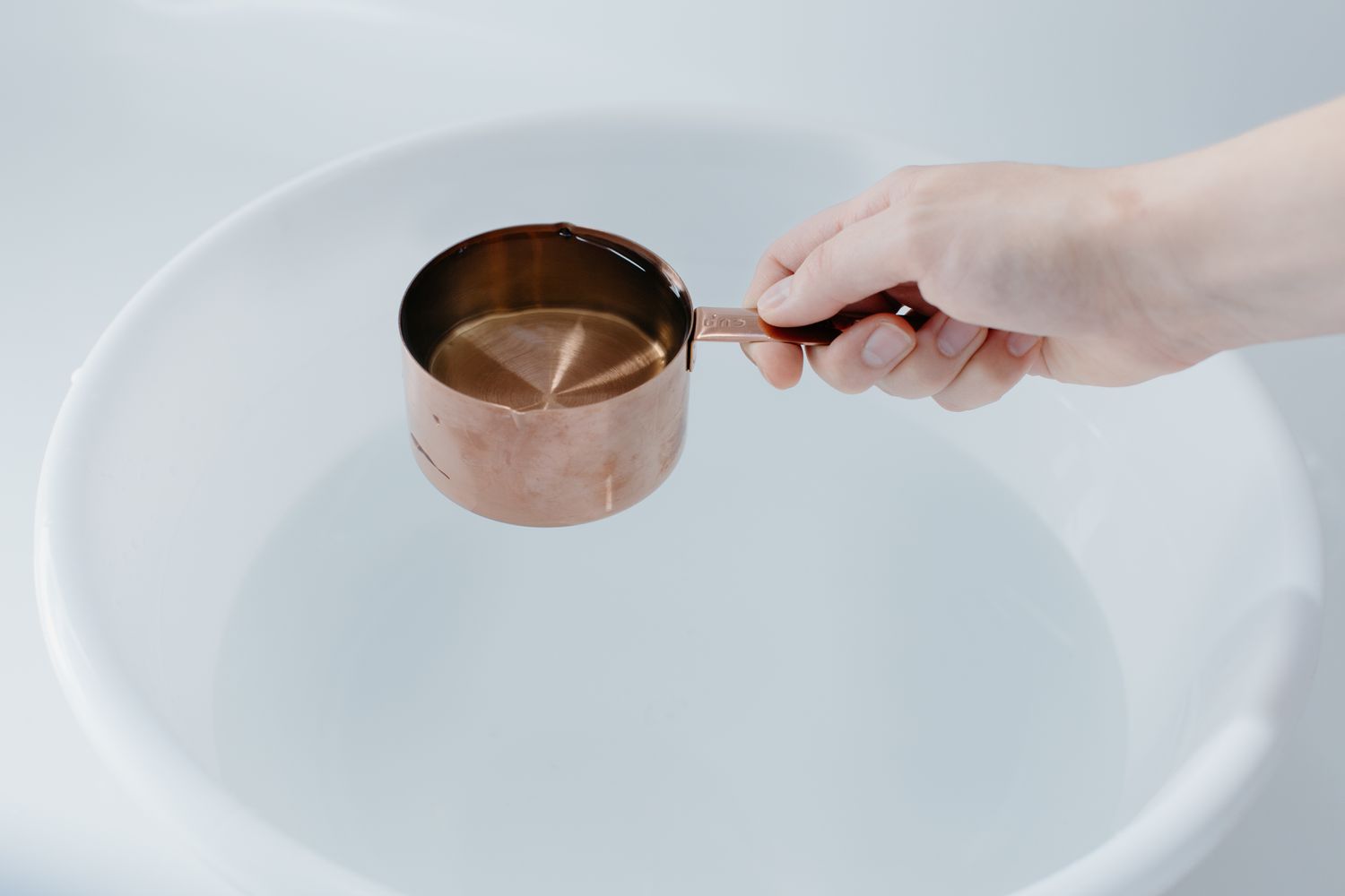 Copper measuring cup scooping water from bucket