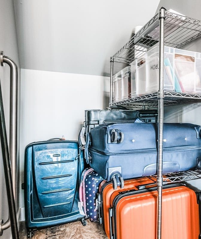 Pequeno armário de armazenamento com paredes inclinadas com uma prateleira de metal empilhada com malas