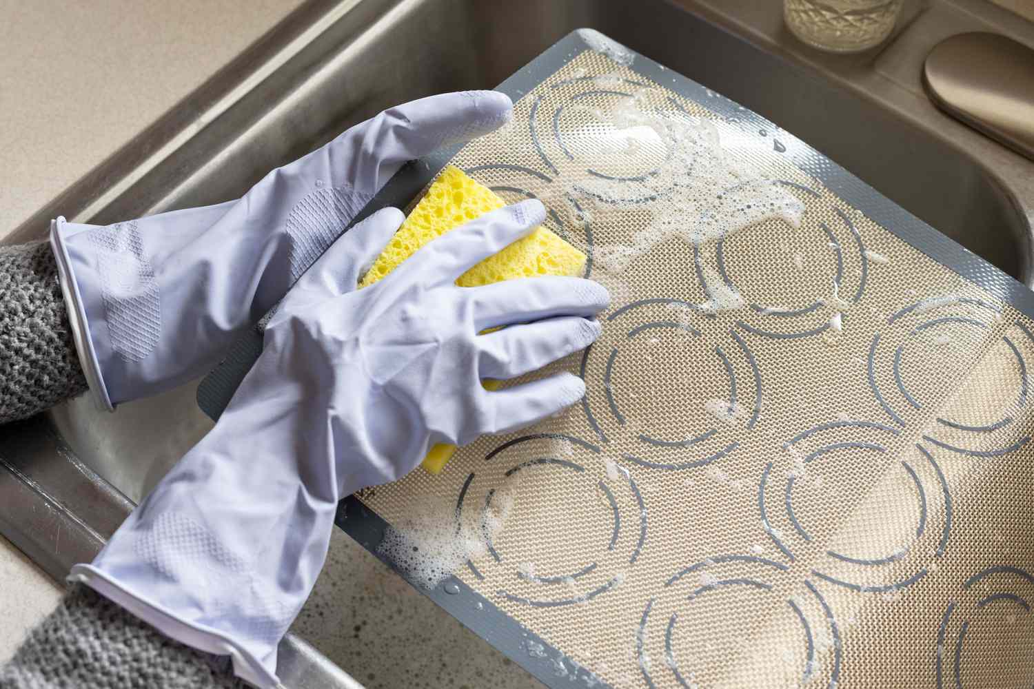 Alfombrilla de silicona para hornear limpiándose con jabón para platos y esponja en el fregadero de la cocina