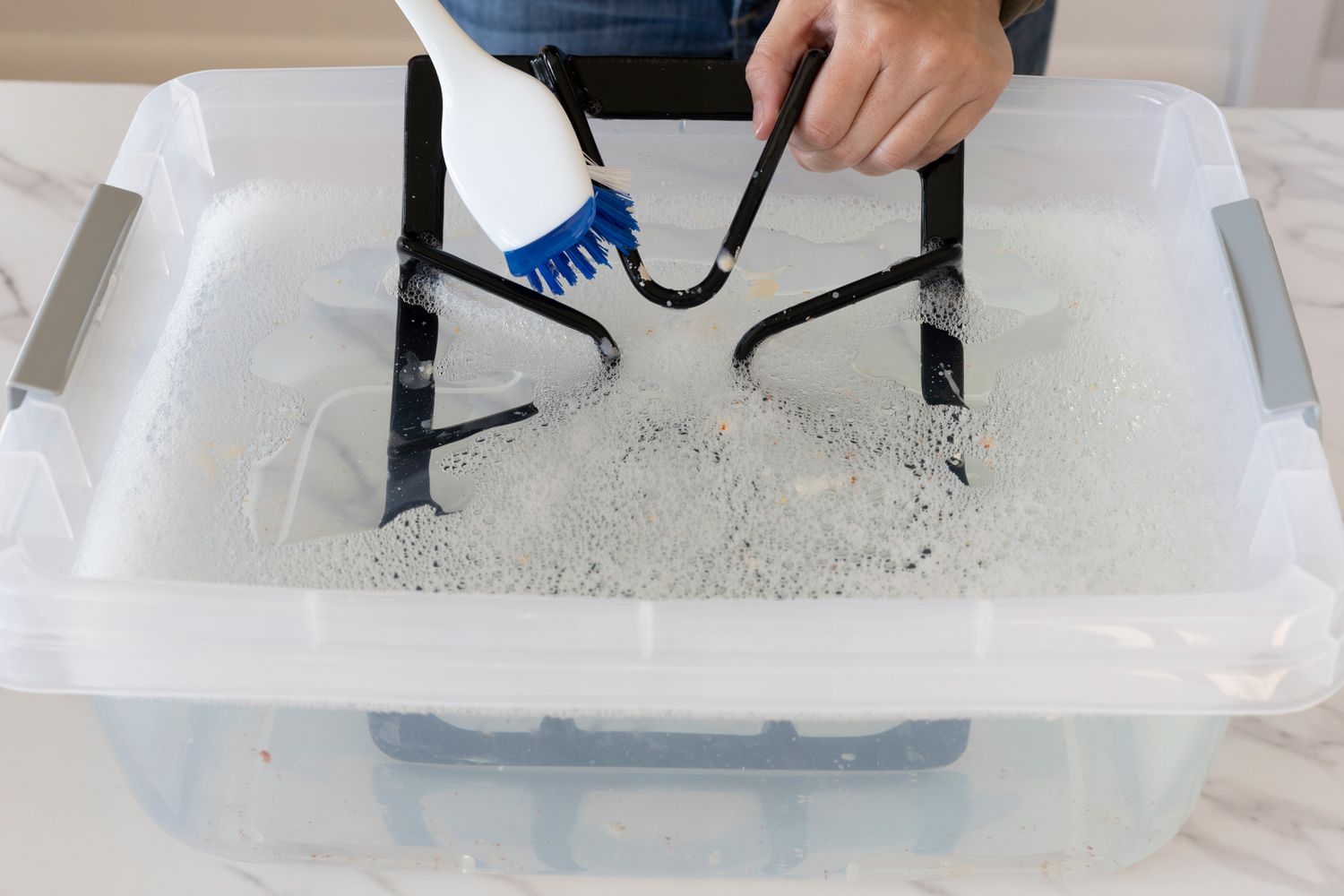 Escova de nylon com cerdas duras esfregando a grelha do fogão em um balde com água e sabão