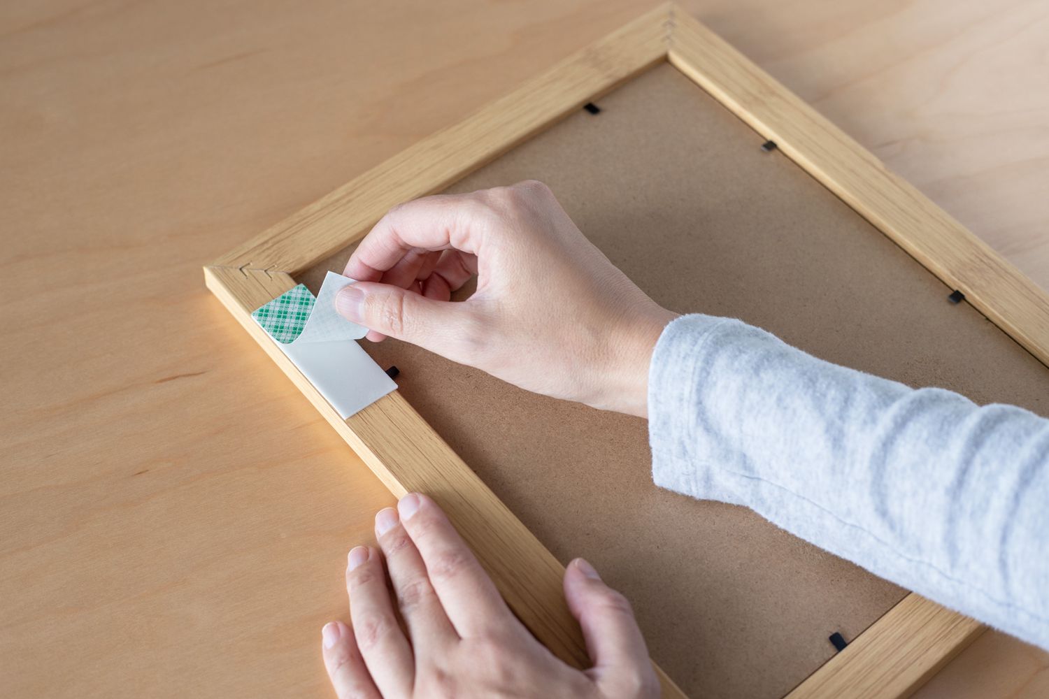 Back of wooden picture frame with double-sided tape cover being removed