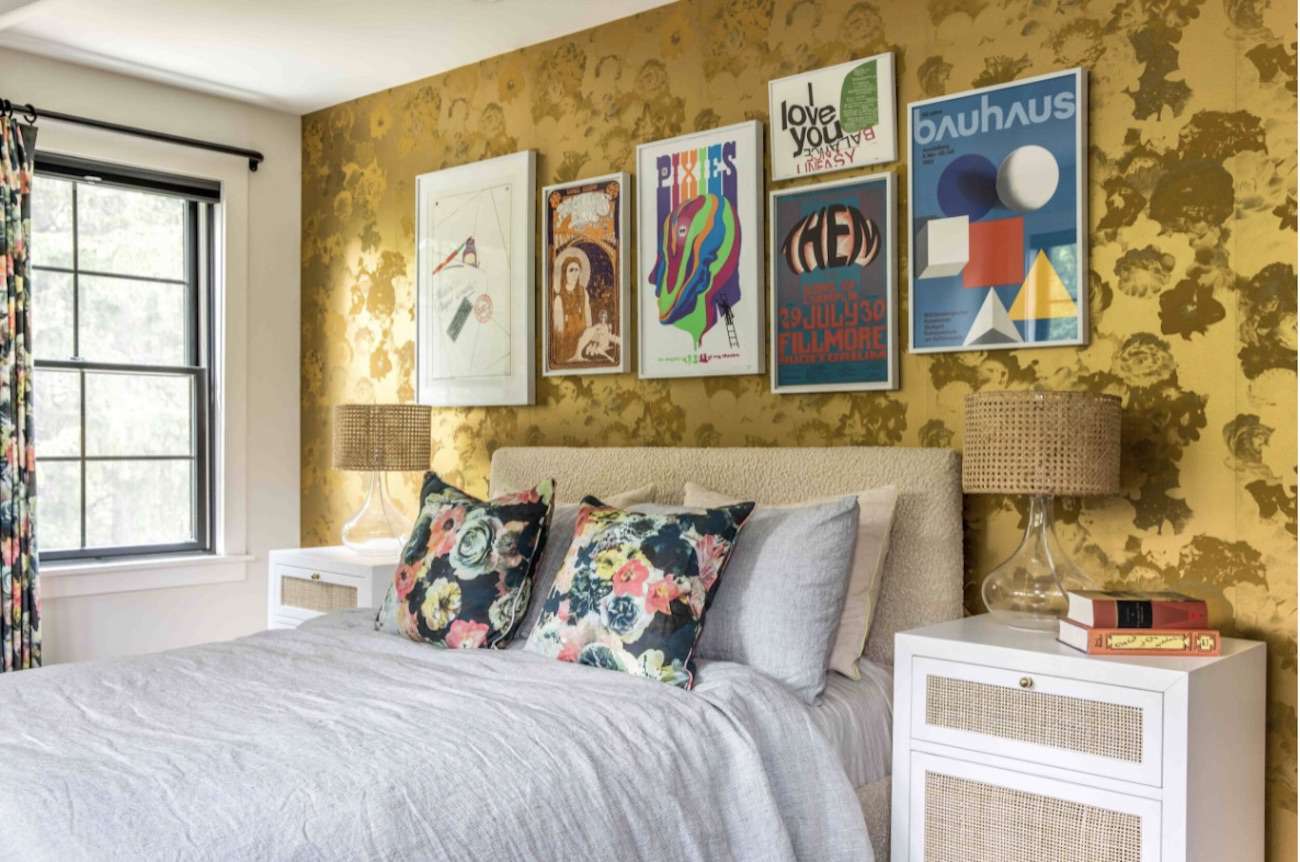 quarto com parede de destaque em folha floral amarela, gravuras emolduradas penduradas acima da cama, travesseiros e cortinas florais 