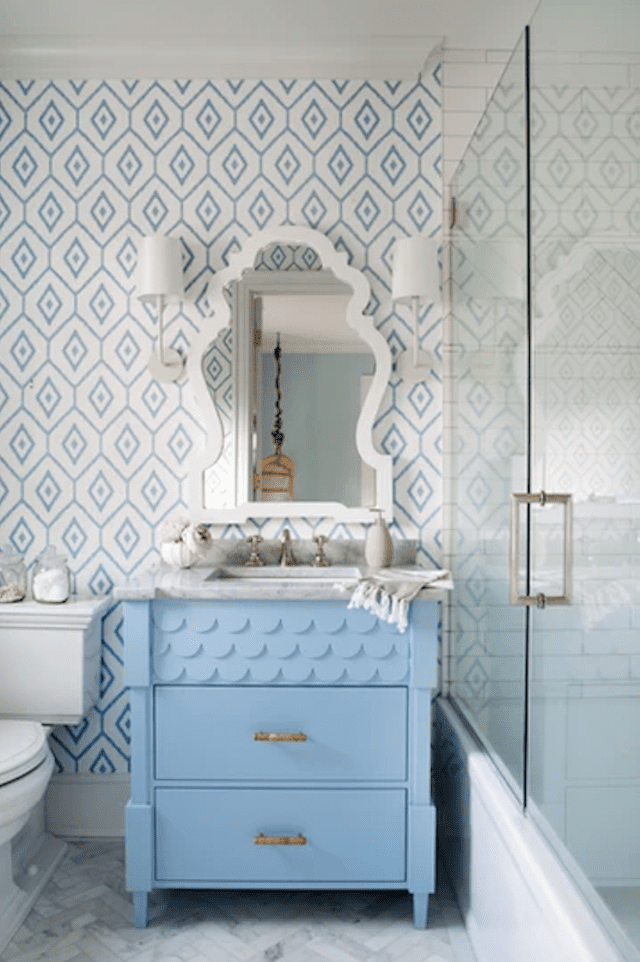 Tocador azul con espejo blanco encima en una pared empapelada en azul y blanco