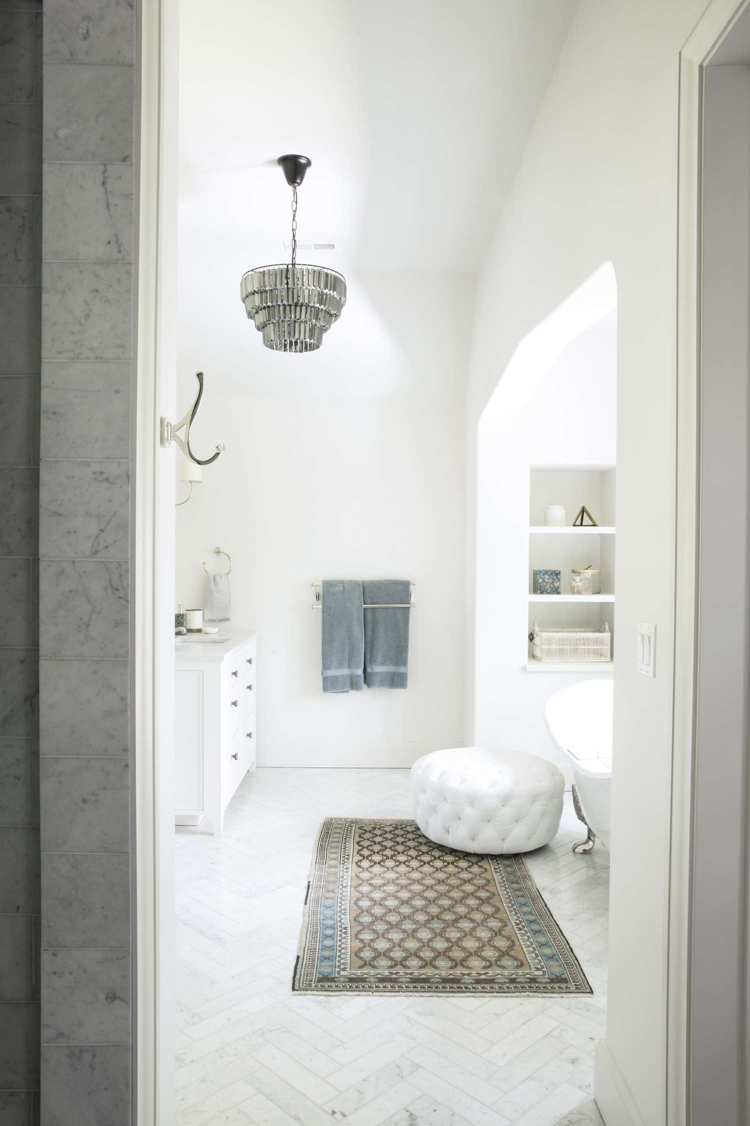 Ein großes Badezimmer mit weißem Ottoman, Teppich und silbernem Kronleuchter