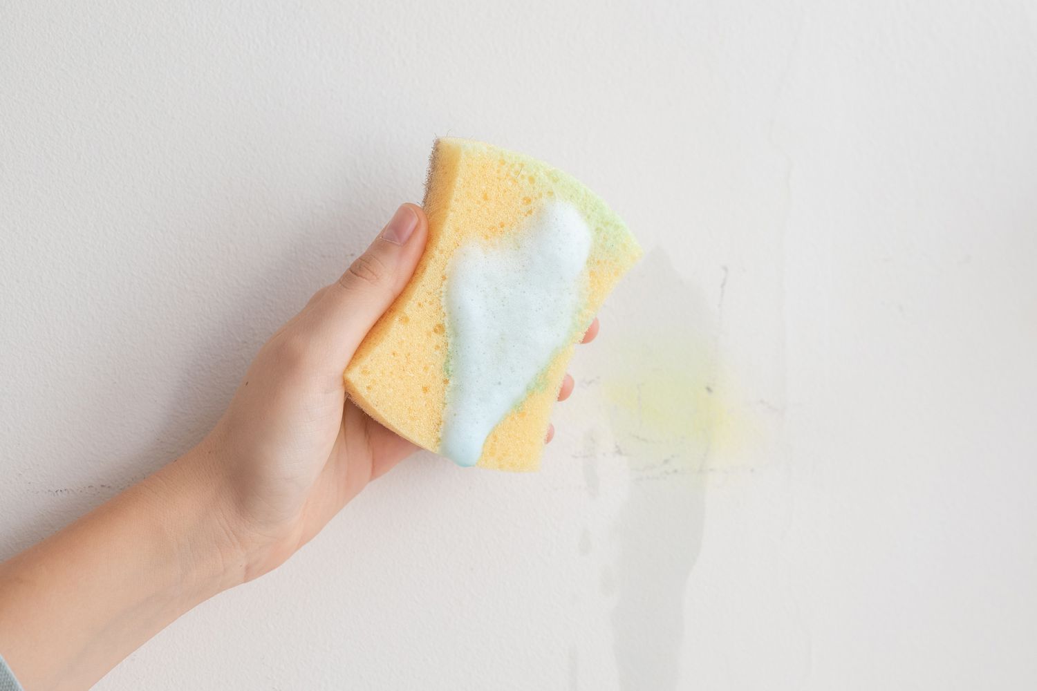 Limpador multiuso com espuma de sabão em uma esponja amarela para limpar uma parede branca