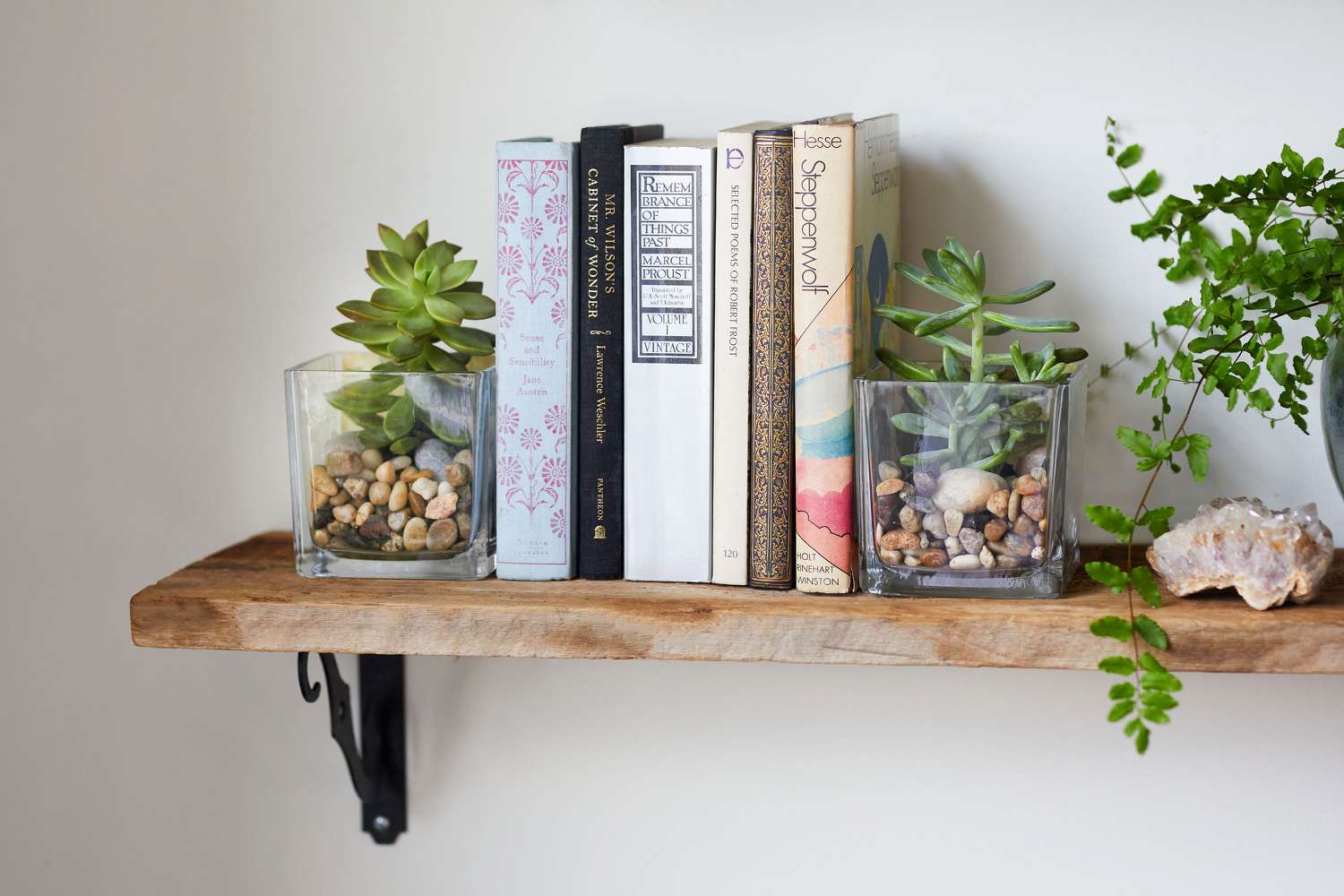 Serre-livres DIY réalisés avec des vases en verre clair, des galets et des succulentes sur une étagère en bois