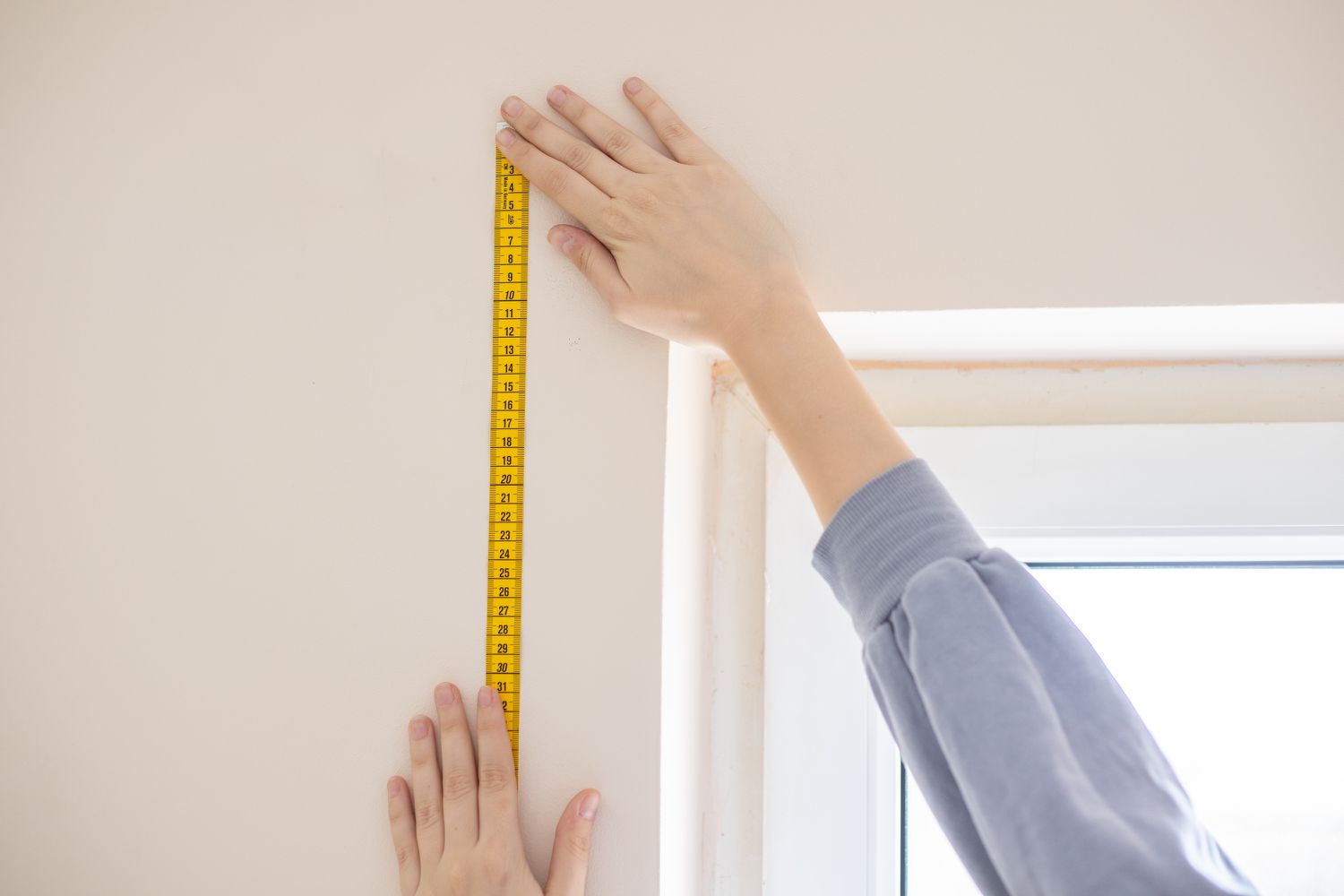 Medición de la altura de la ventana con cinta métrica amarilla para persianas