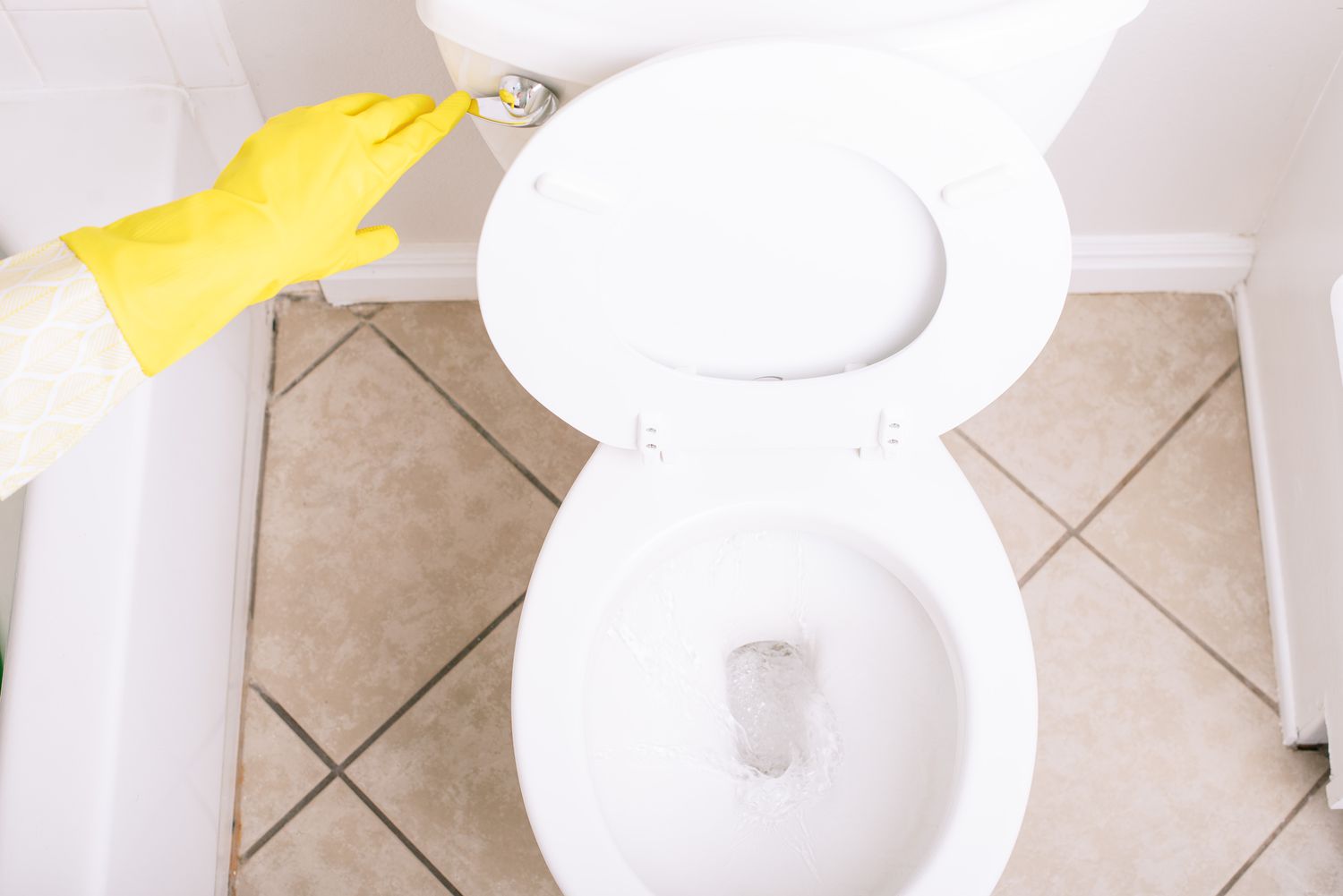 Vaso sanitário de cerâmica branca recebendo descarga manual com luvas amarelas