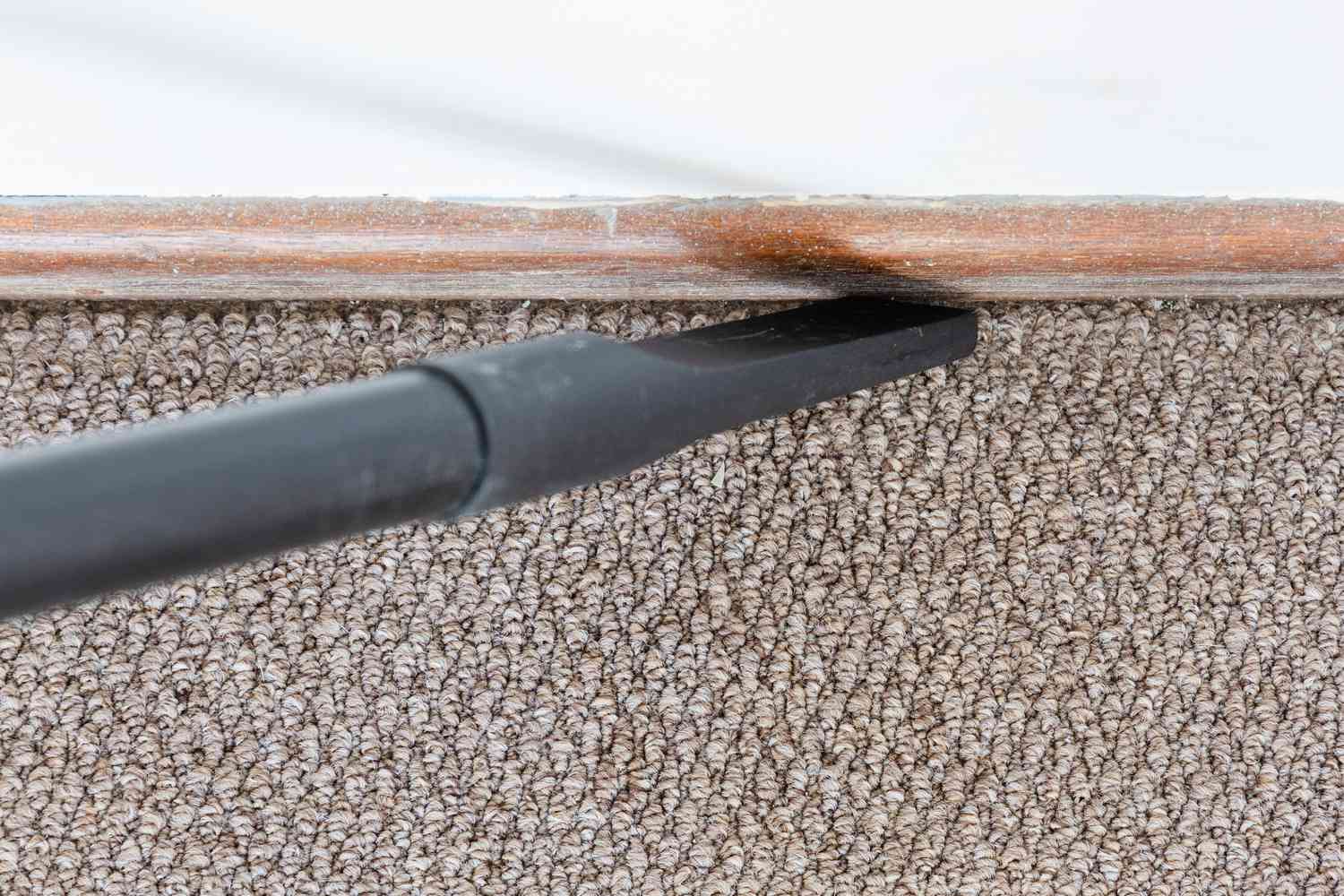 Staubsaugerspitze beim Reinigen des Spalts zwischen Teppich und Sockelleiste