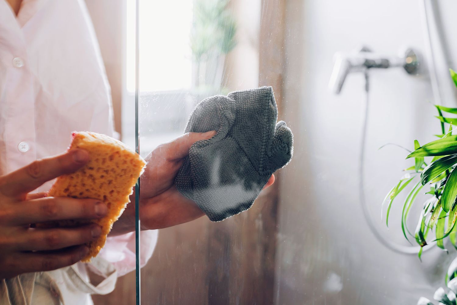 Pano de microfibra cinza secando a porta de vidro do chuveiro após borrifar a solução de amônia e água