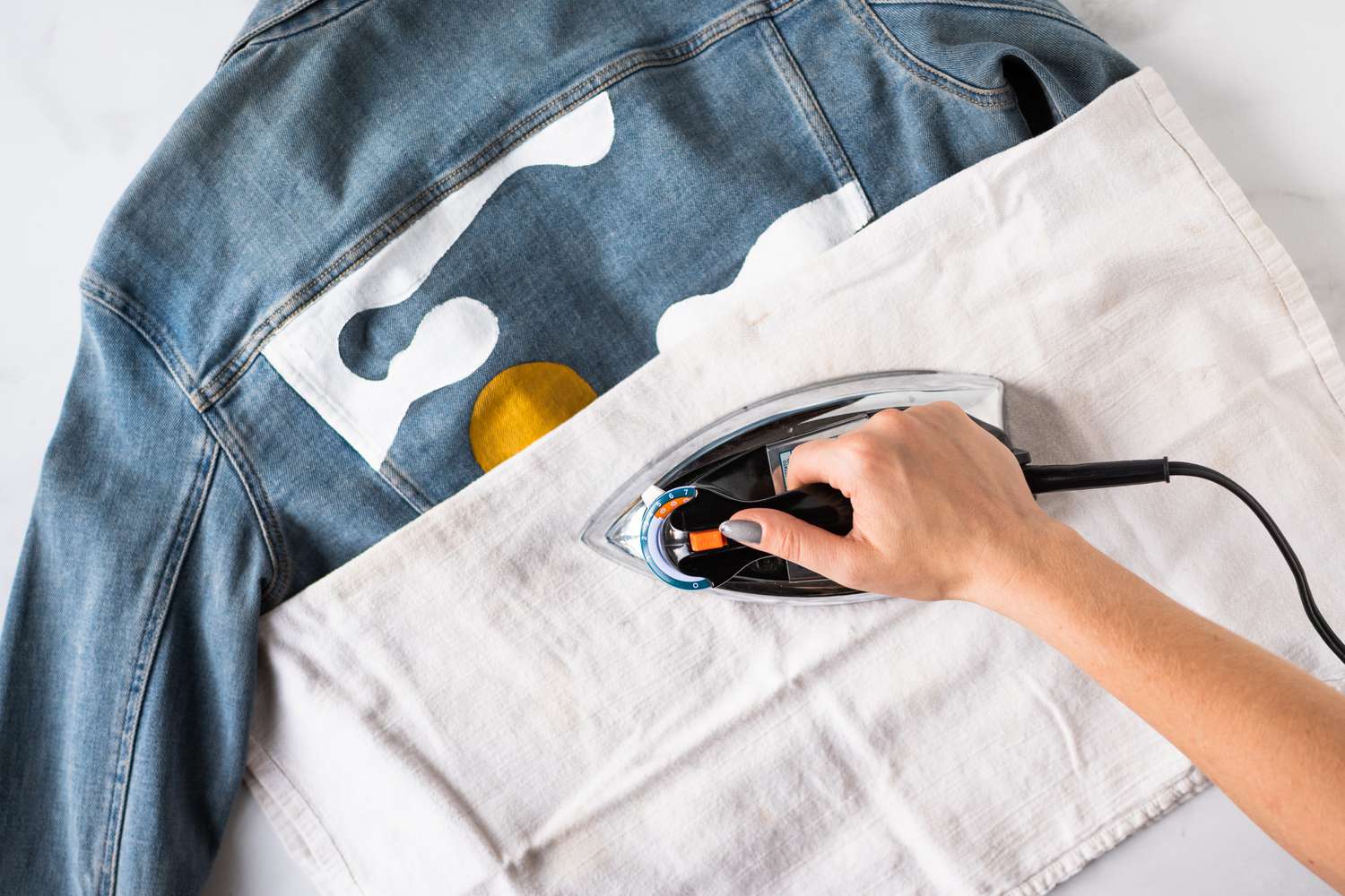 Bügeleisen fährt über ein gemaltes Landschaftsmotiv auf der Rückseite eines Jeansstoffs mit einem Baumwolltuch dazwischen