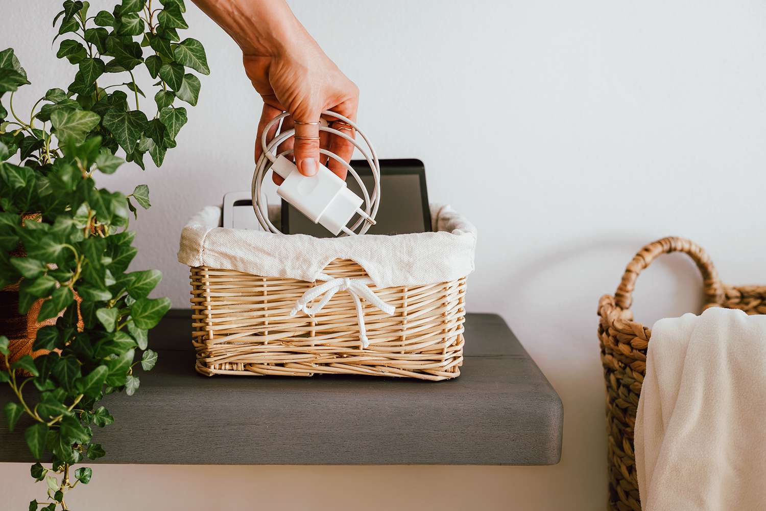 Wrapped charging cord placed in small basket with smart devices next to plant
