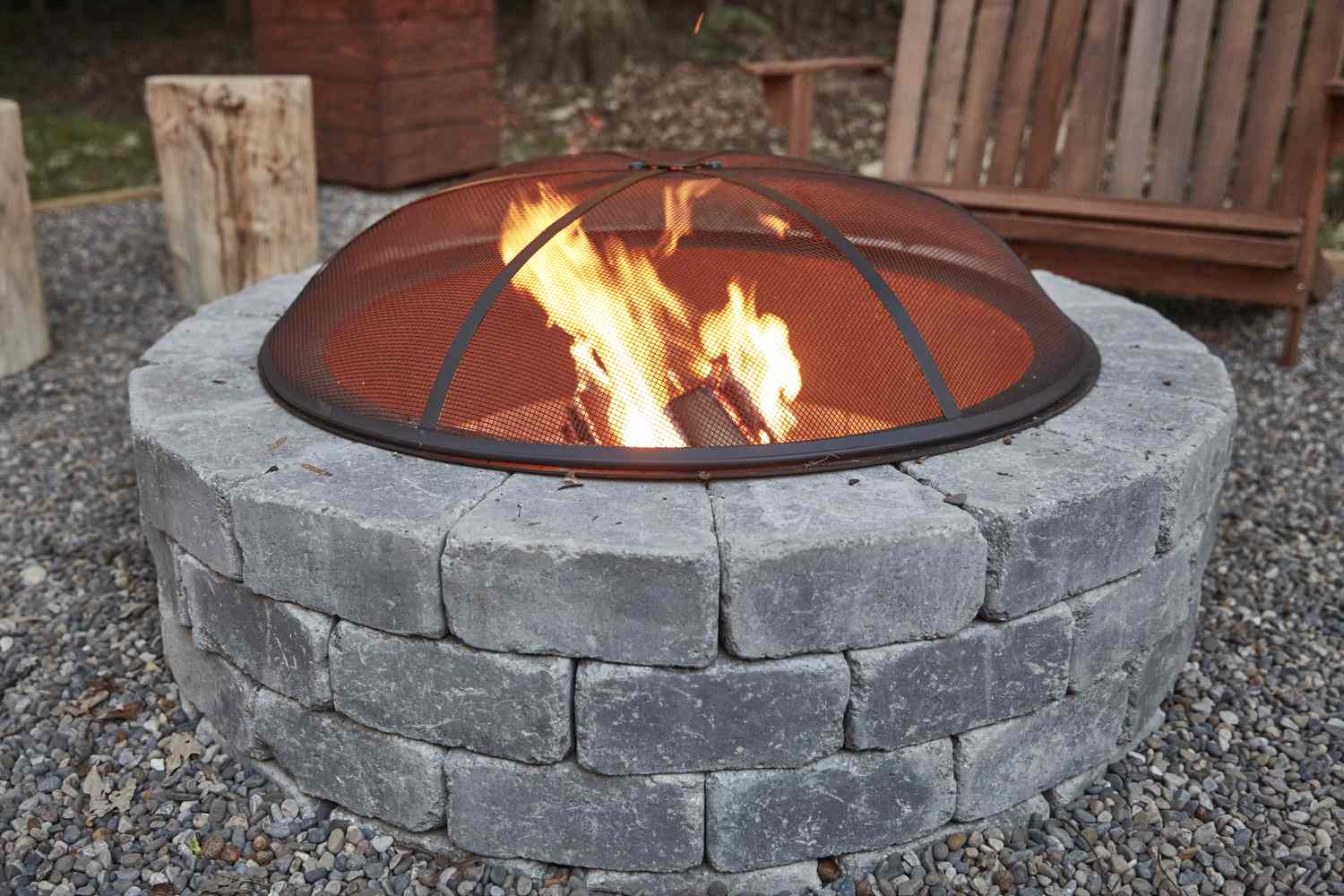 Kreisförmige Feuerstelle aus grauen Steinen mit Schutzabdeckung über dem Feuer