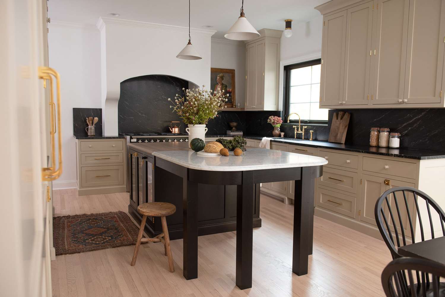 Eine Küche im europäischen Stil mit einer großen Insel und beigen Schränken mit einer schwarzen Marmorplatte als Aufkantung.