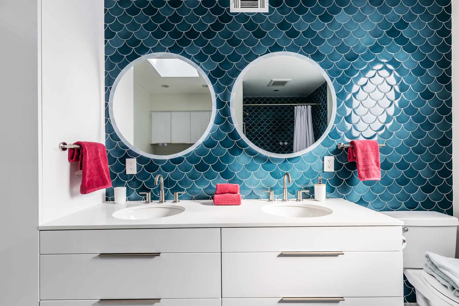 Salle de bain pour enfants avec des murs bleus en forme d'écailles de poisson avec des miroirs circulaires et des serviettes rouges