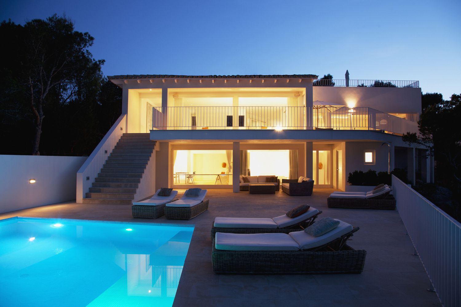Una piscina de agua salada por la noche con una casa iluminada cerca.
