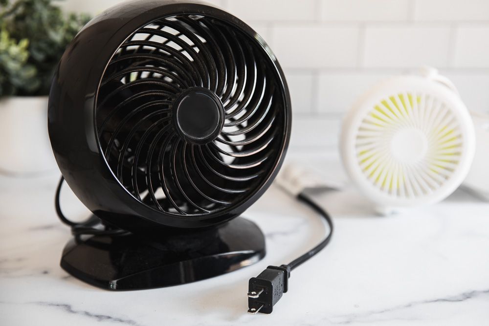 Ventilateur de comptoir noir débranché de la prise murale à côté d'un petit ventilateur blanc