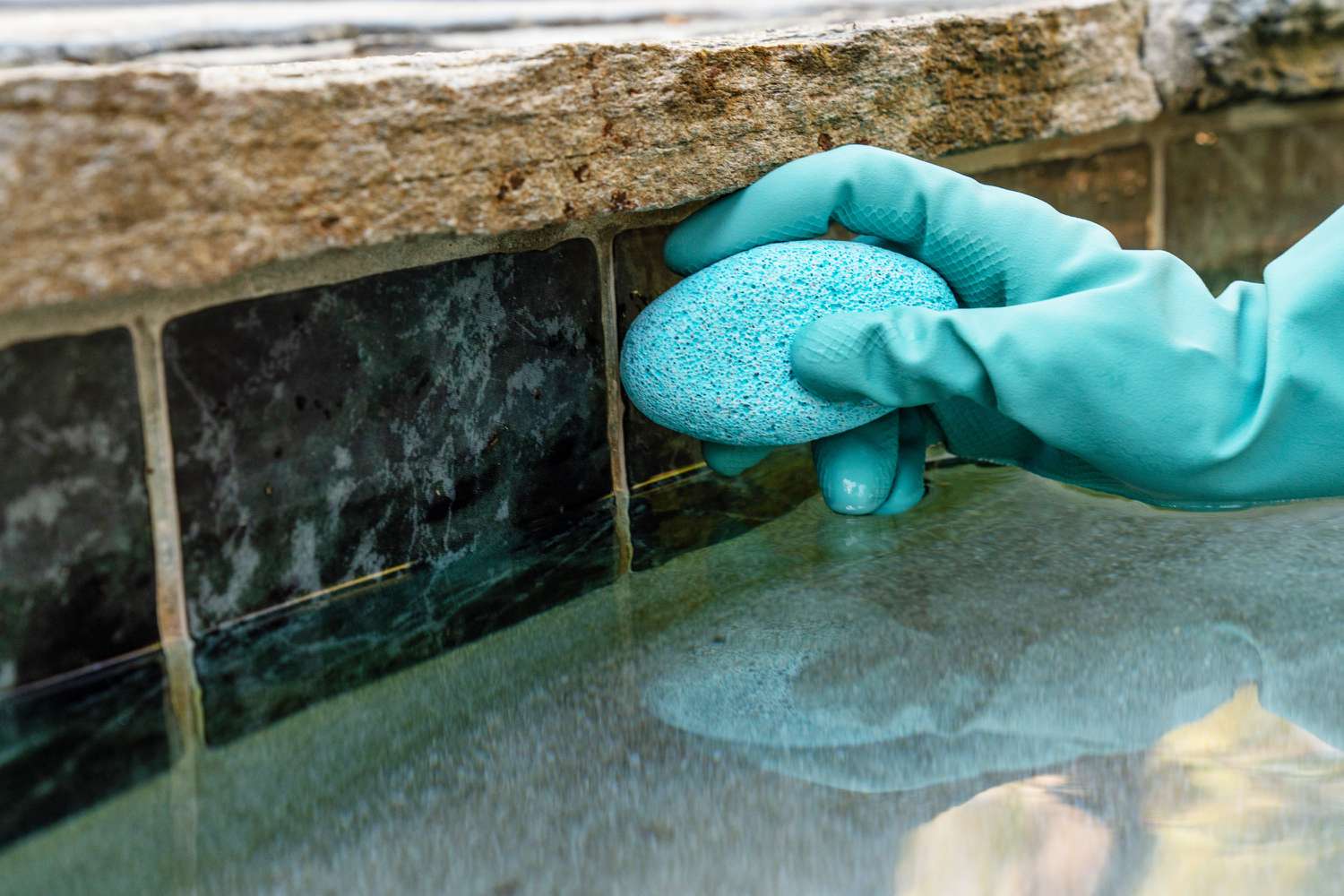 Blauer Bimsstein, der an den Poolfliesen reibt, um mineralische Ablagerungen zu entfernen