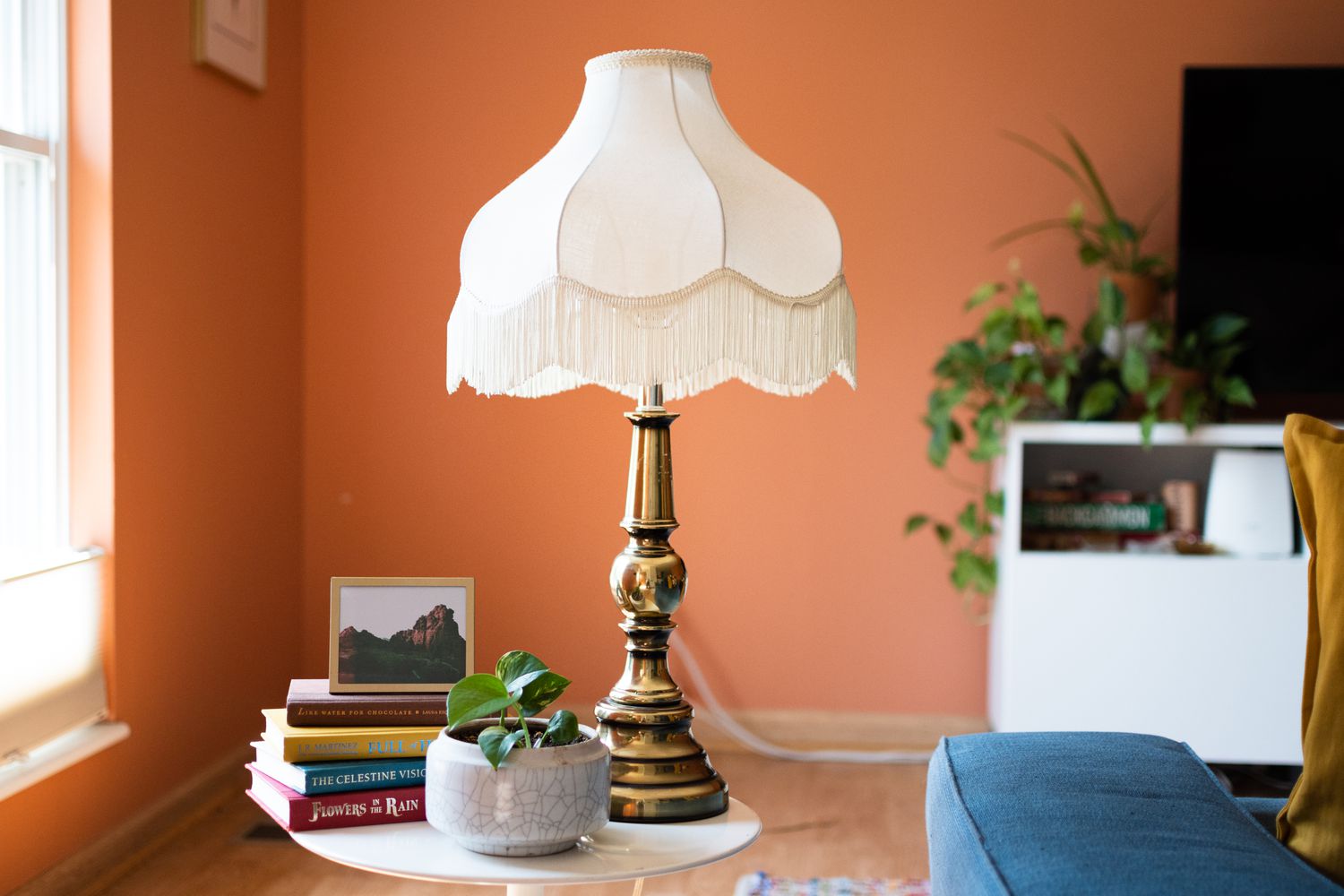 Abat-jour blanc épuré avec franges sur lampe dorée sur le dessus de la table d'appoint avec livres et plantes d'intérieur