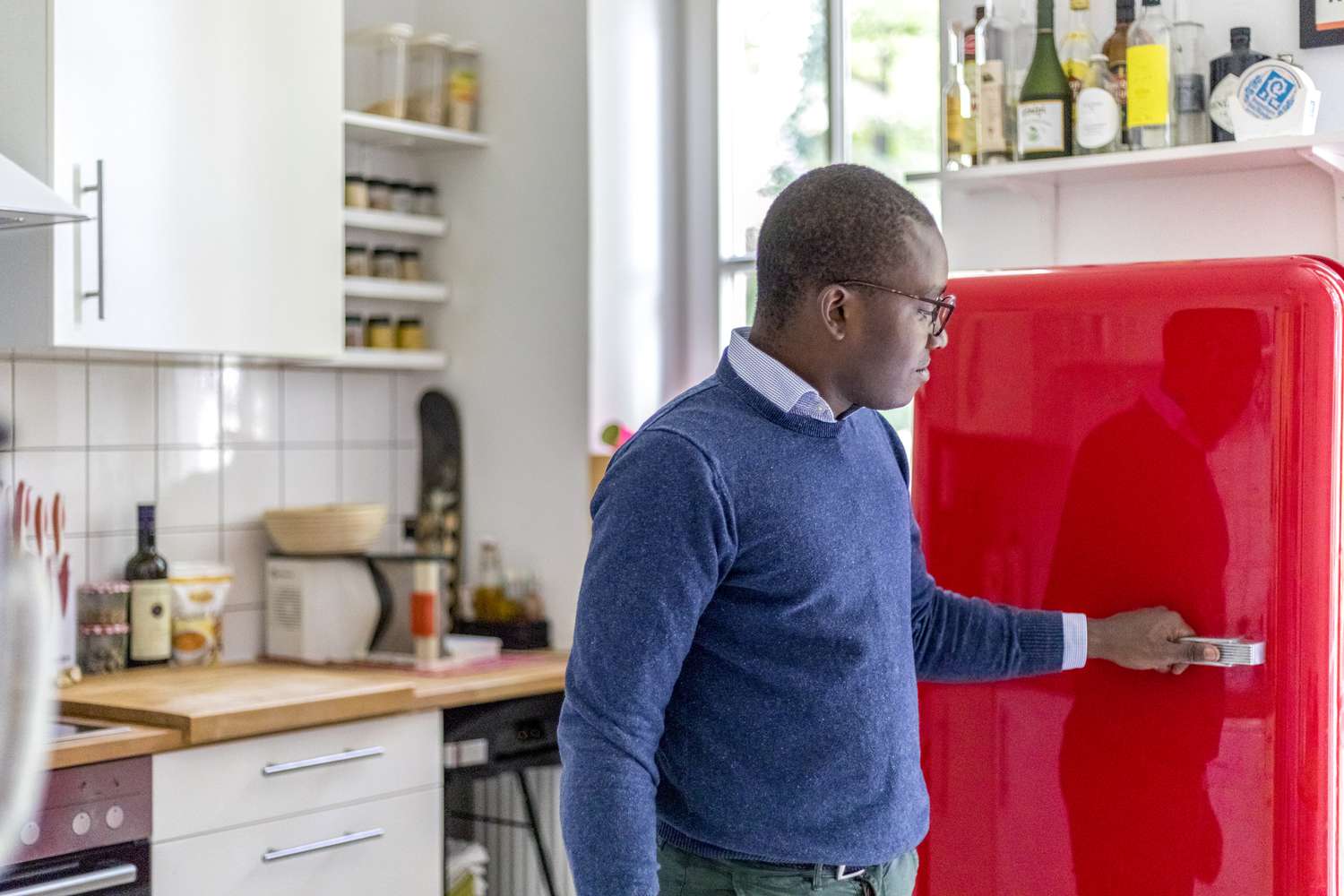 Homem abrindo uma geladeira vermelha.