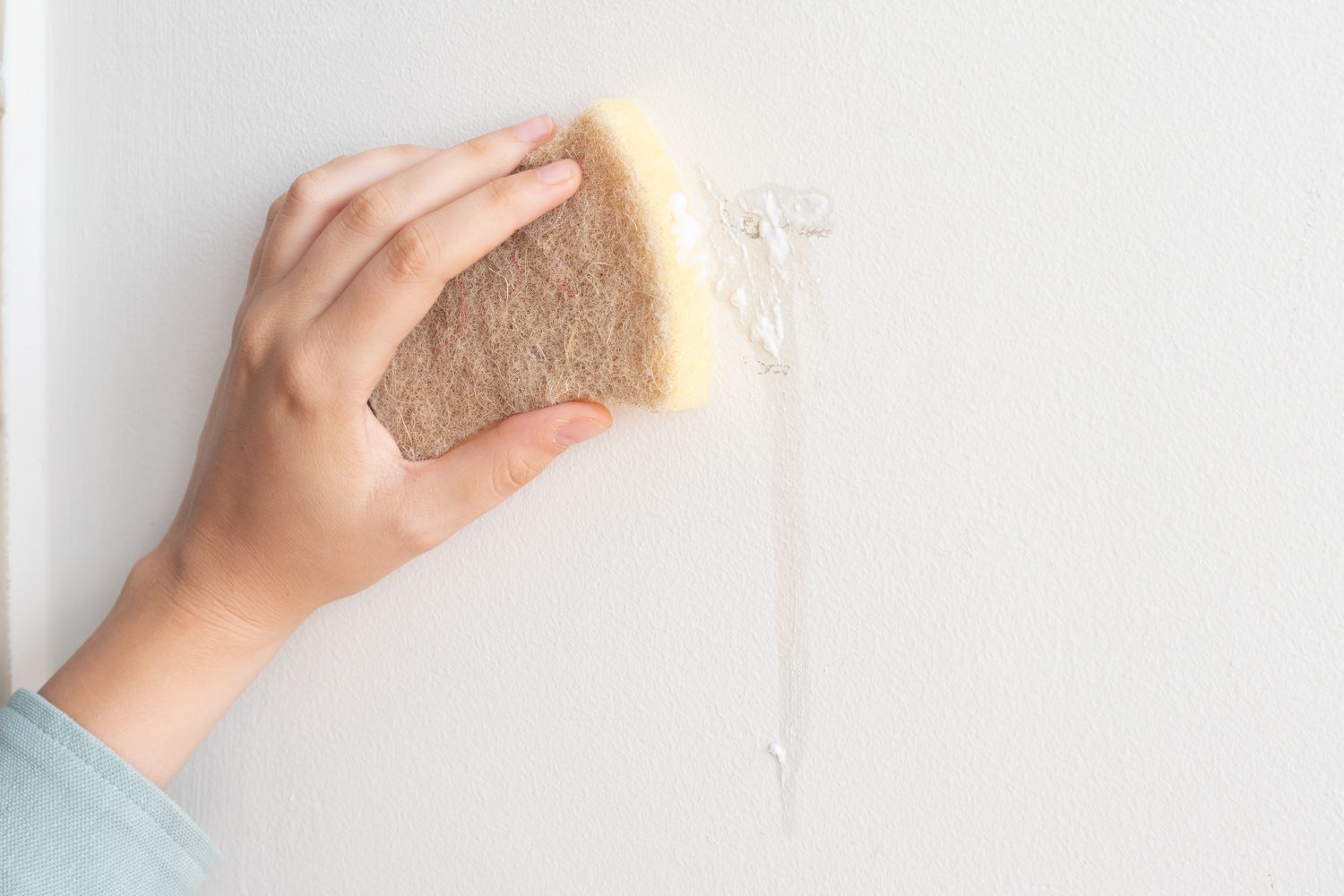 Weicher Schwamm schrubbt Spülmittel auf weißer Wand, um Flecken zu entfernen