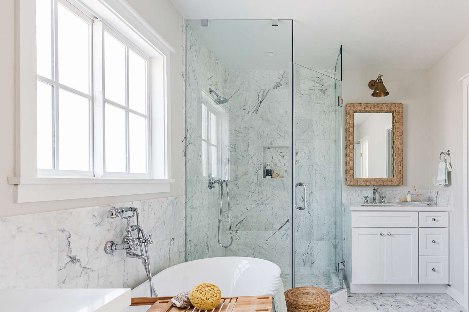 Porte de douche en verre dans une salle de bain marbrée blanche avec baignoire blanche et grande fenêtre