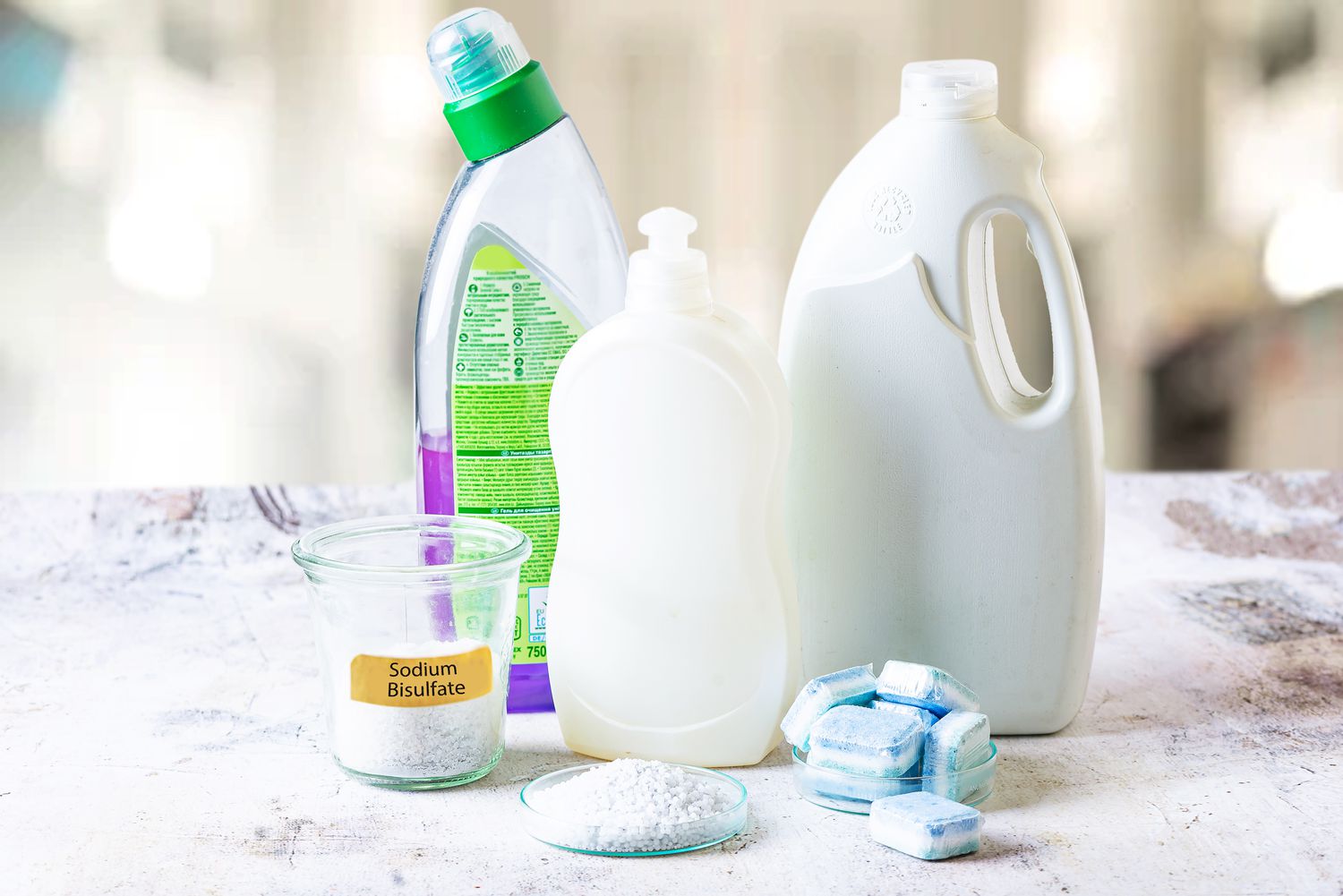 Natriumbisulfat-Pellets in einem Glasbehälter neben Haushalts- und Geschirrspülerflaschen