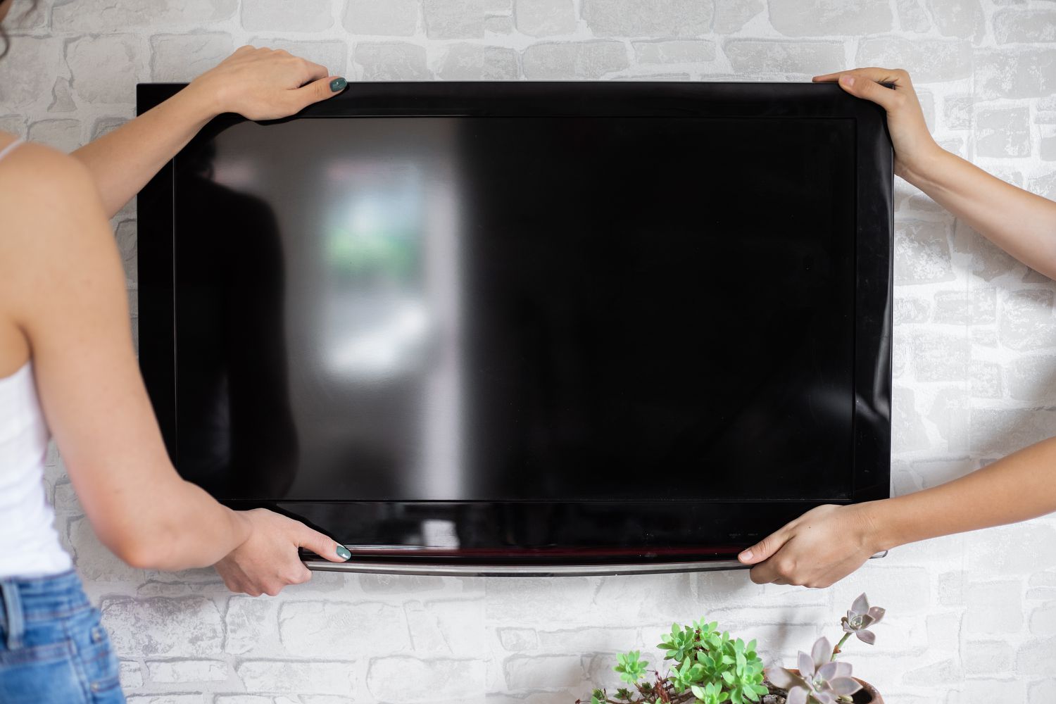 Flachbildfernseher mit zwei Händen an der Montageplatte an der Wand befestigt