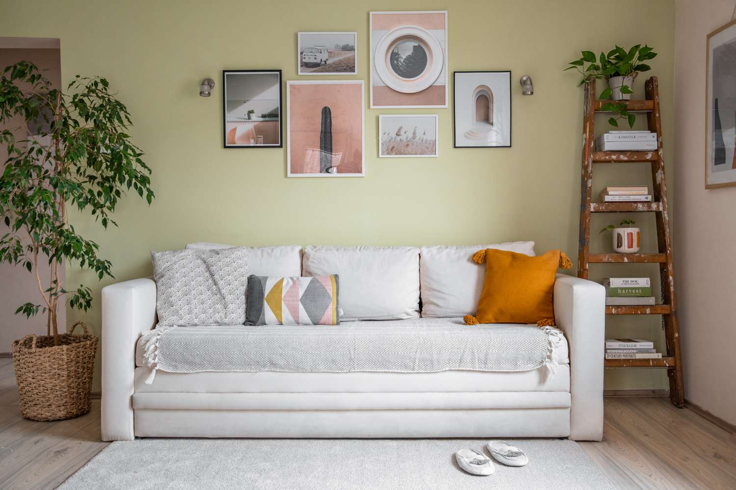 Weiße Couch mit selbstgemachten Bezügen und Überwurfdecke obenauf im grünen Wohnzimmer