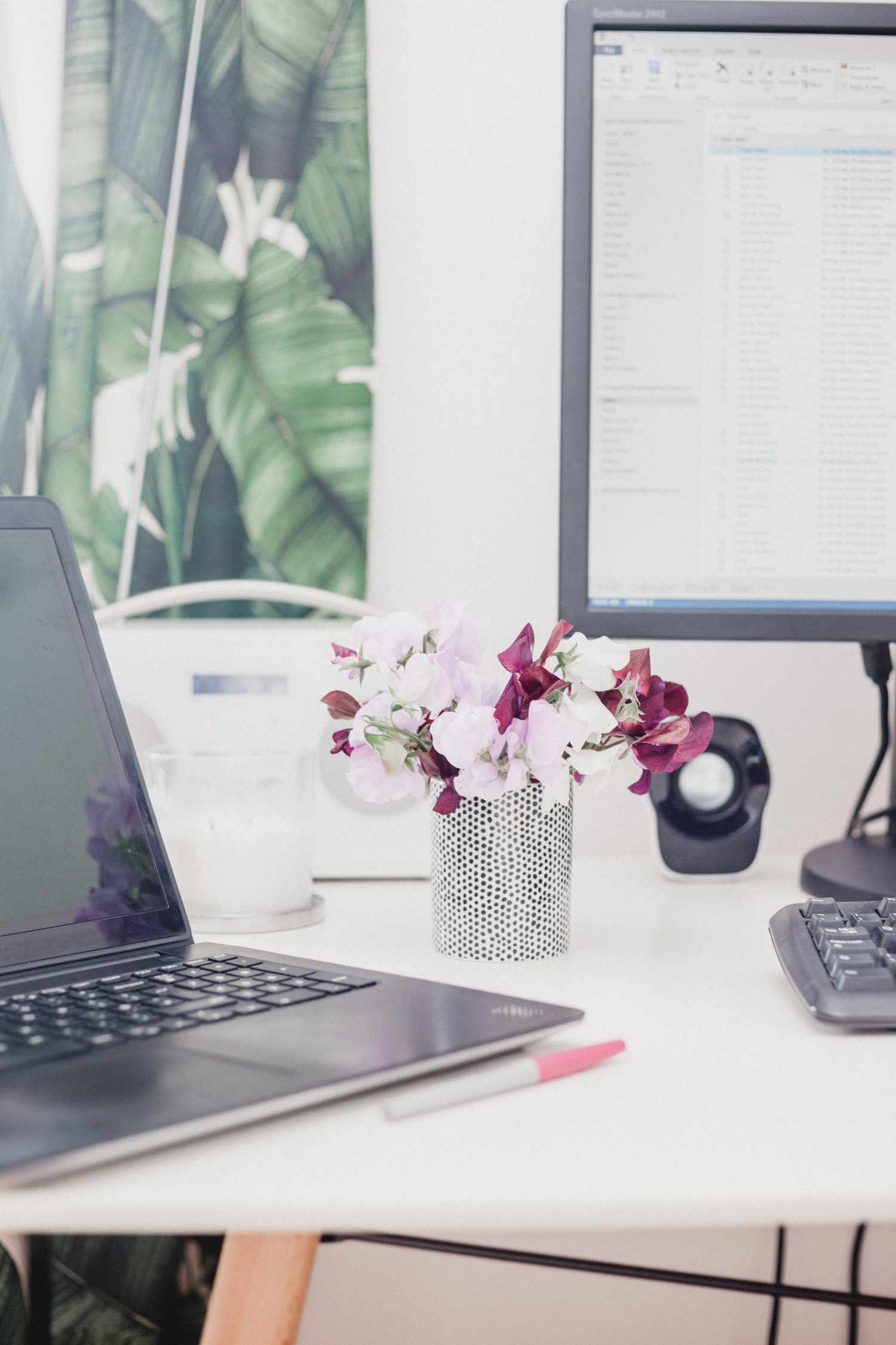 Nahaufnahme von Schreibtisch mit Laptop, Monitor und Blumen