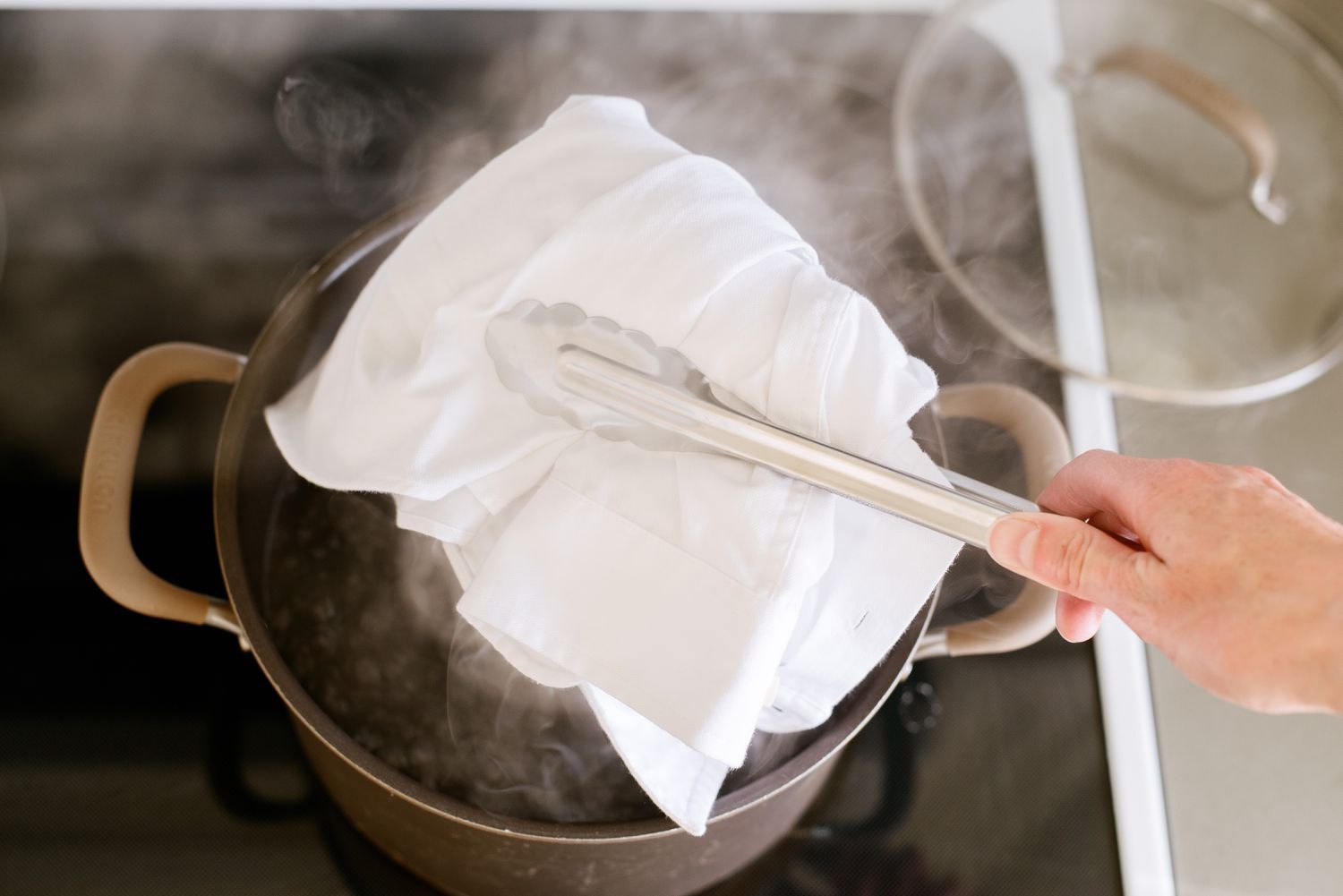 Weißes Hemd zum Schrumpfen mit einer Metallzange in den Kochtopf gegeben