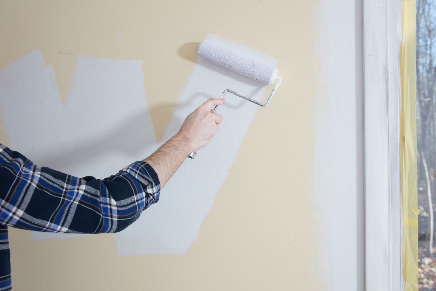 Rolo de pintura aplicando tinta branca em traços diagonais na parede